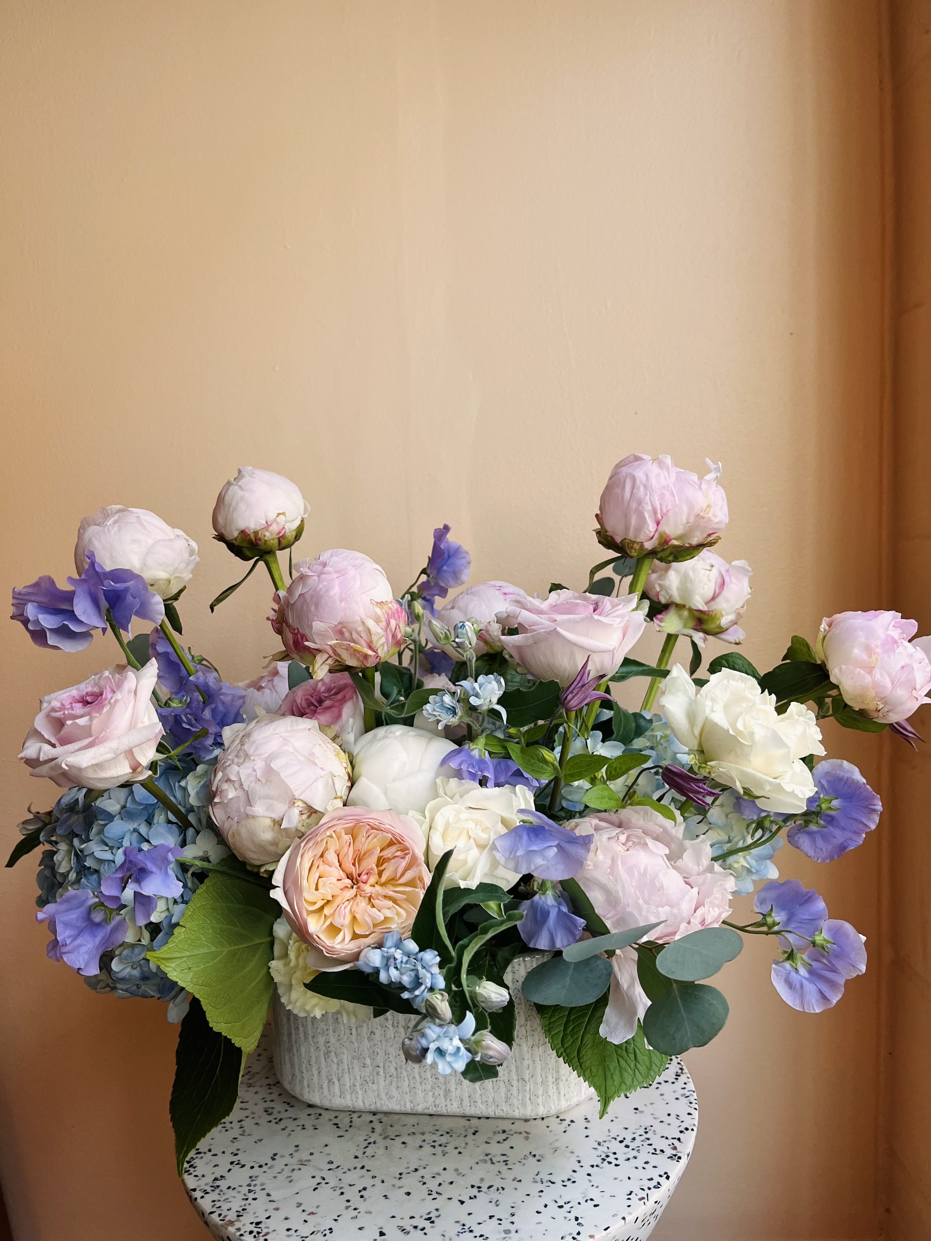 Pastel bouquet of roses, peonies, and blue flowers in a white vase