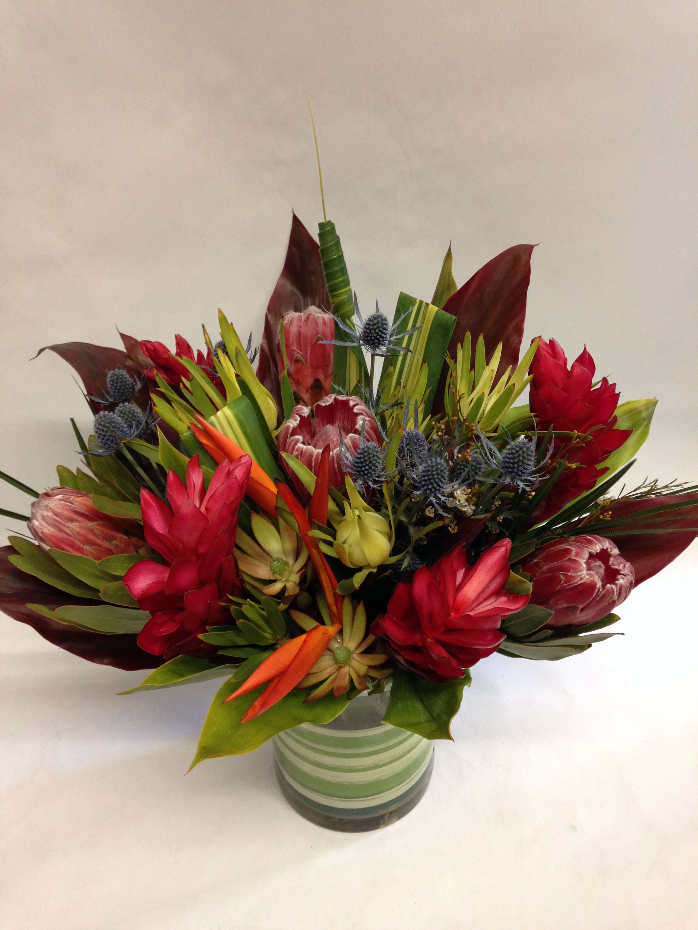 Hawaiian Paradise (Pre-order) - This tropical arrangement comes complete with king proteas, safari branches, Birds of Paradise, ginger flowers, sea thistle, ti leaves and other exotic greenery.  (Some flowers may be subject to change depending on the season. We will contact you with available flower substitutions; please contact us with specific questions if you are concerned with flower availability, thanks!)  Featured arrangement: $200.00 (Regular Price)