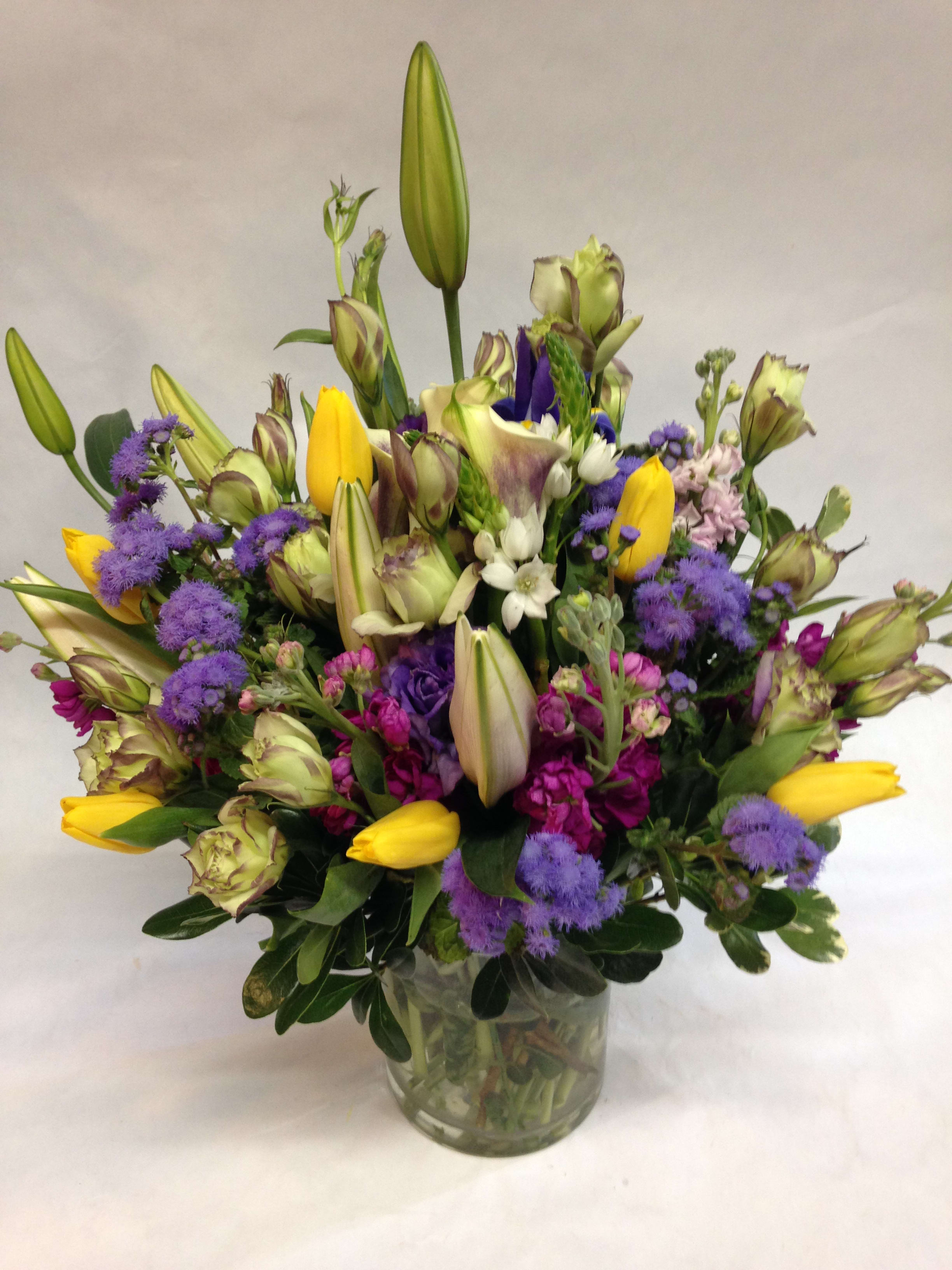 Mixed bouquet of yellow tulips, purple blooms, and lilies in a glass vase