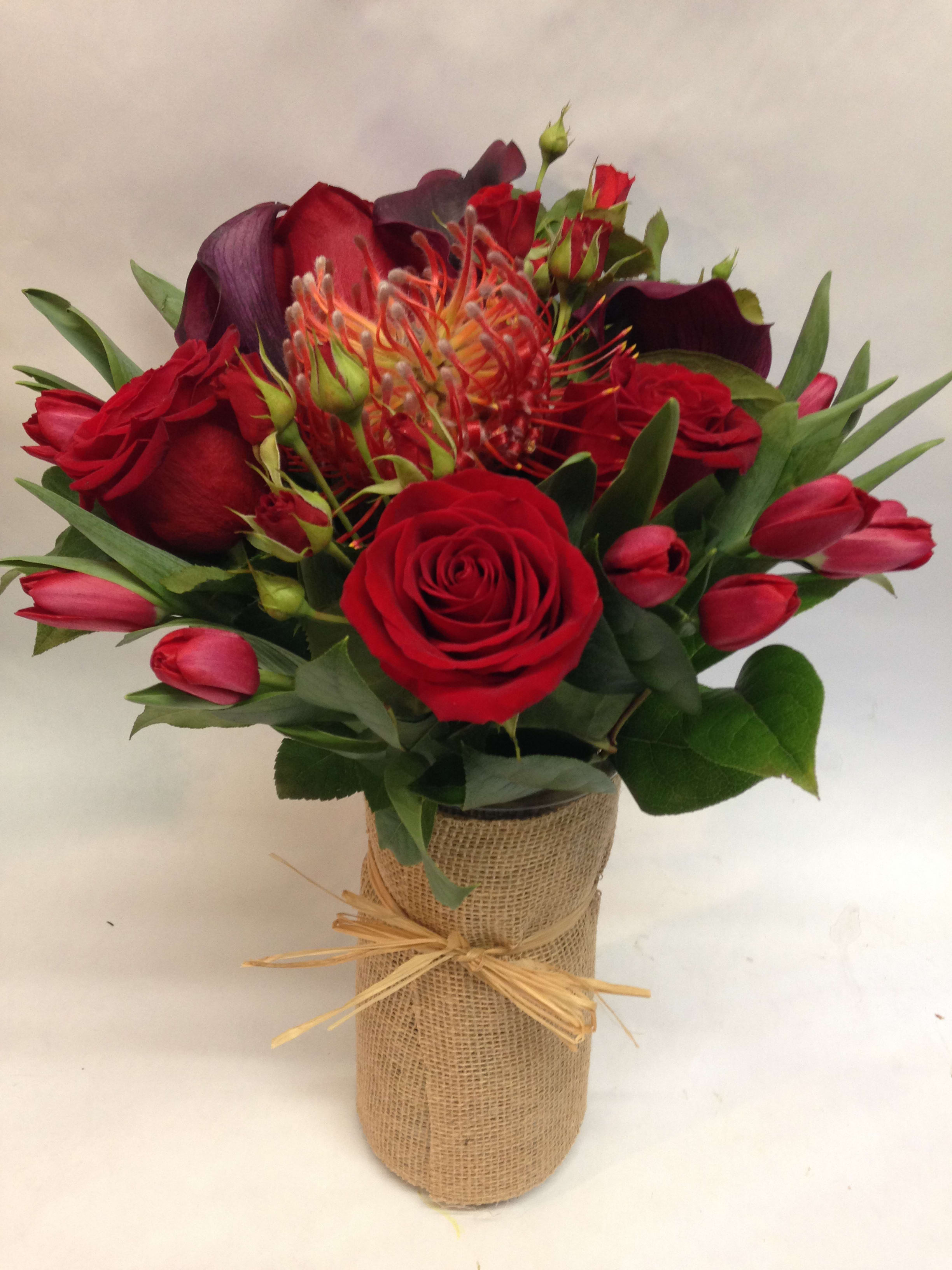 Red With Passion -   This arrangement comes complete with red roses, calla lilies, tulips, pin-cushion proteas and spray roses.  All flowers are assembled in a burlap wrapped vase as well.  (Some flowers may be subject to change depending on the season. We will contact you with available flower substitutions; please contact us with specific questions if you are concerned with flower availability, thanks!)    Featured arrangement: $175.00 (Regular Price)