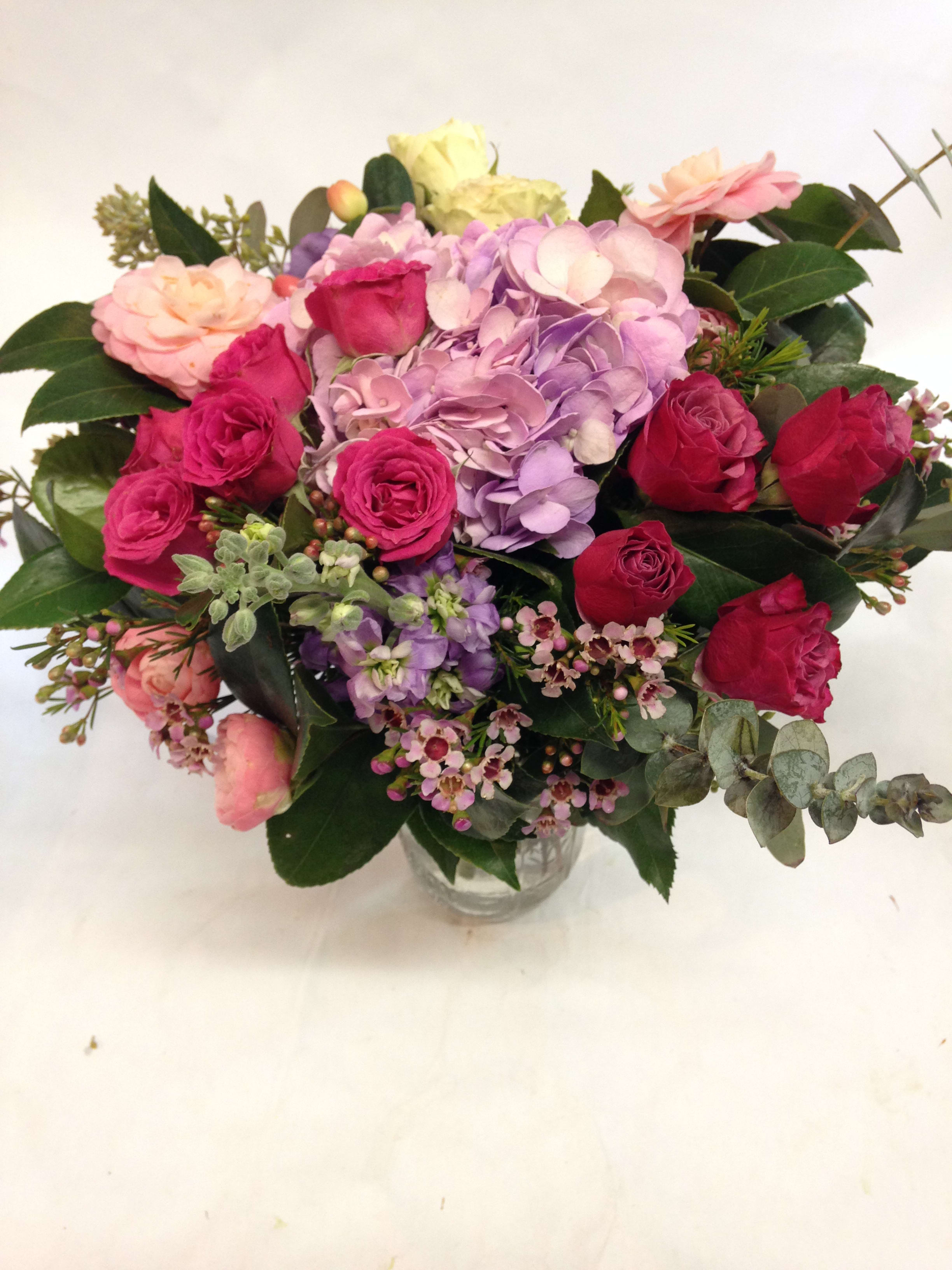 Mixed pink, purple, and red roses in a clear glass vase