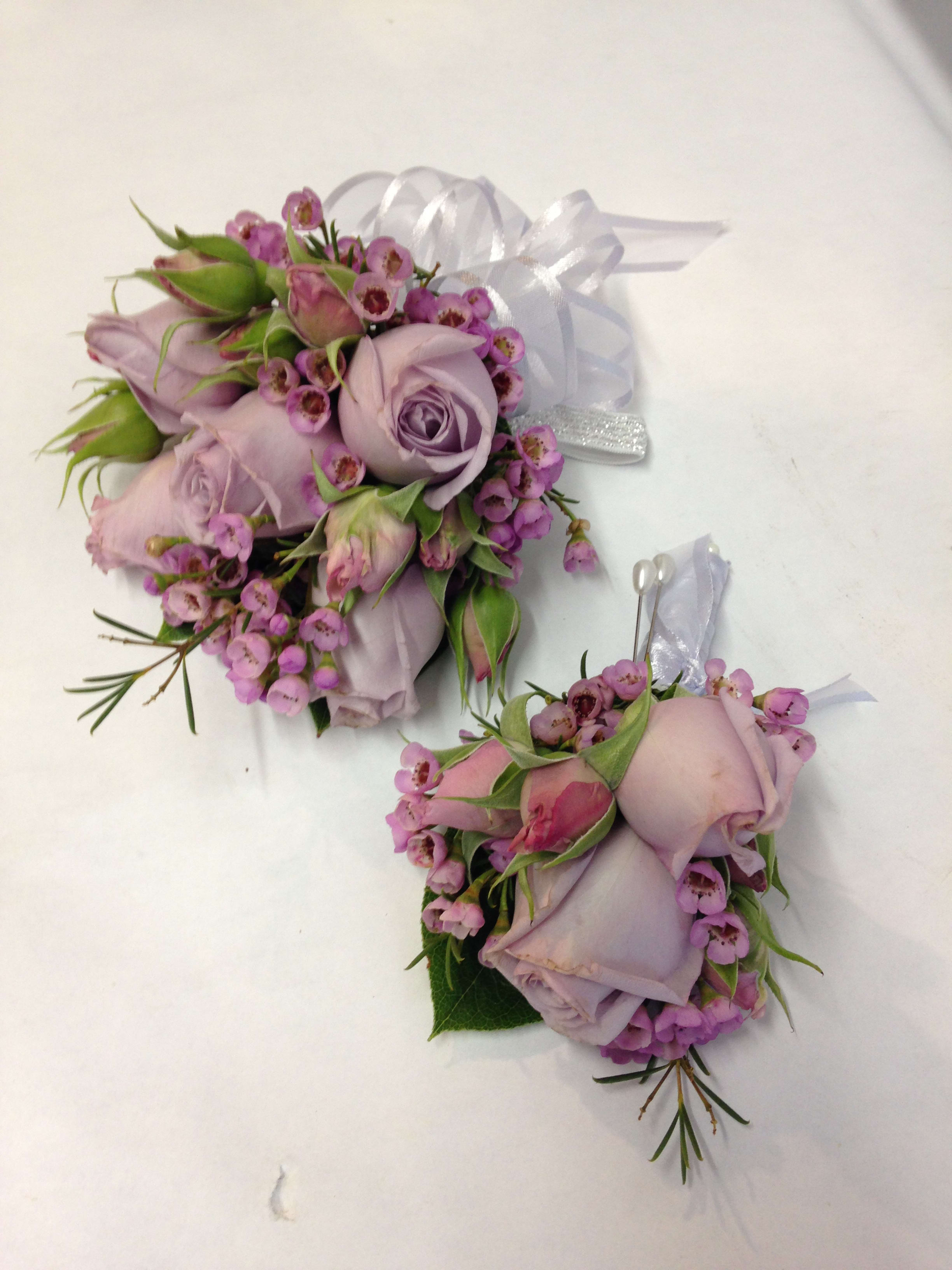 Two lavender rose corsages with pink filler flowers and white ribbon