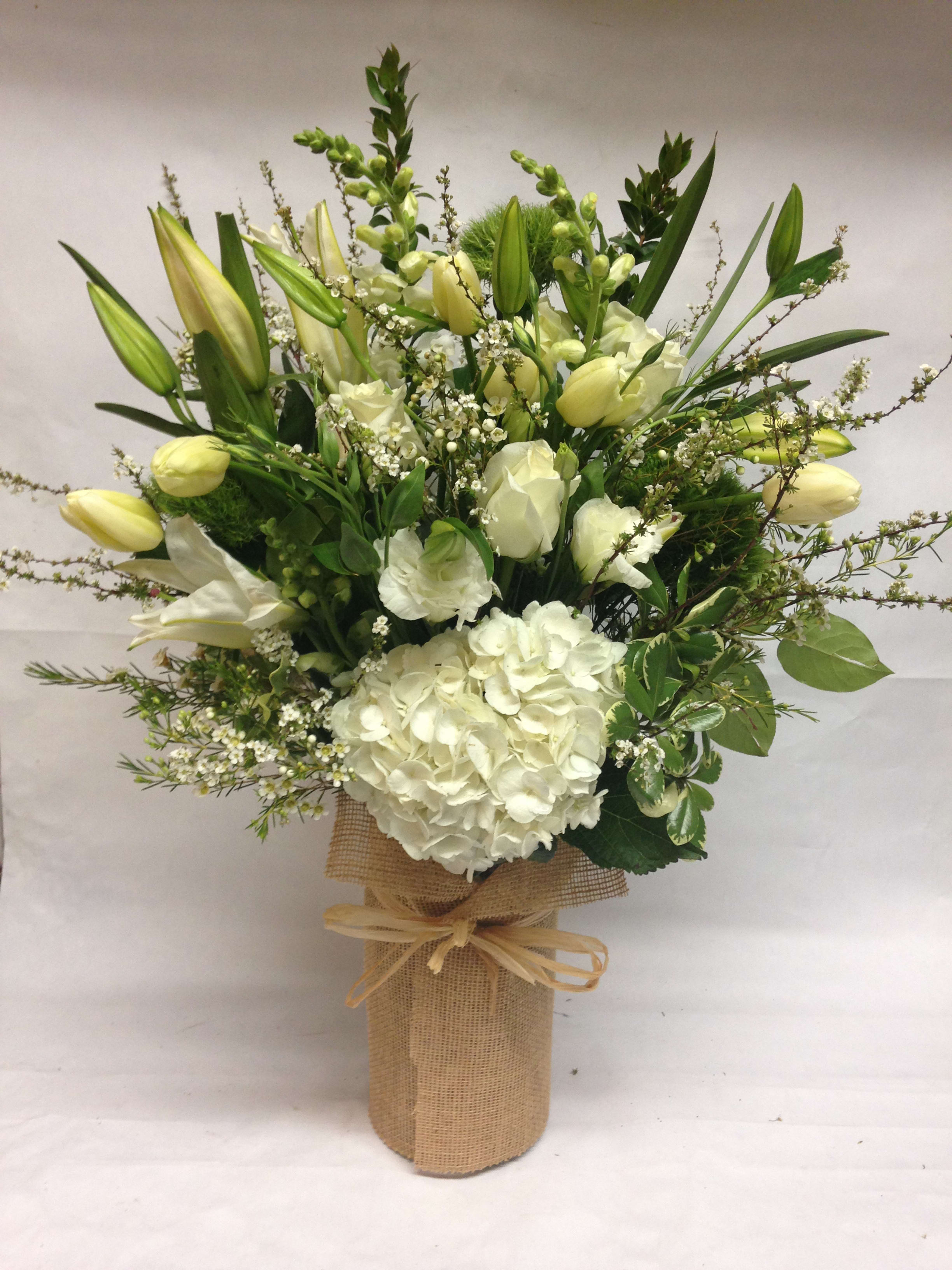 White floral arrangement with lilies and hydrangea in a burlap-wrapped vase