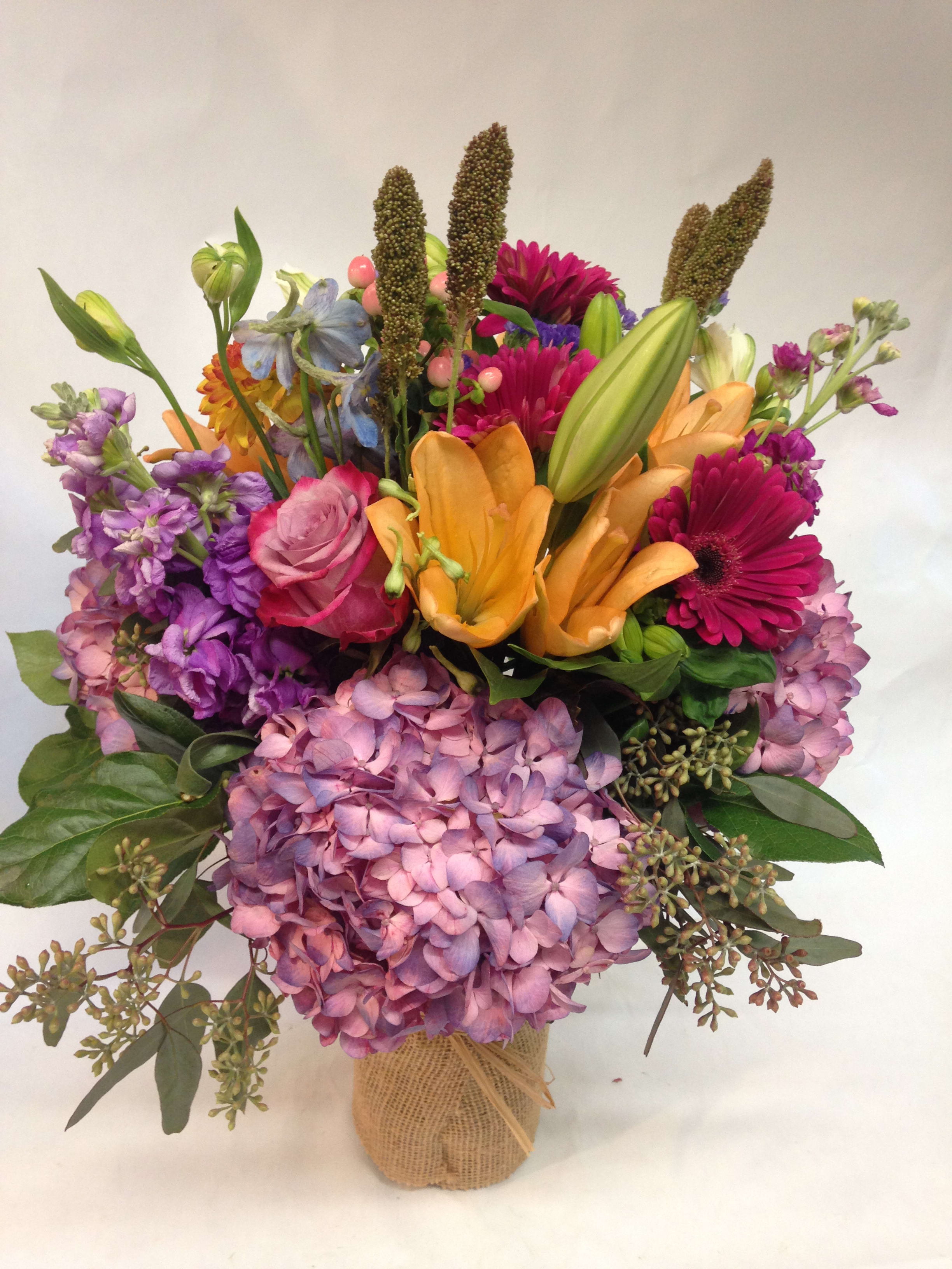 Mixed bouquet with pink hydrangeas, orange lilies, and magenta daisies in burlap wrap