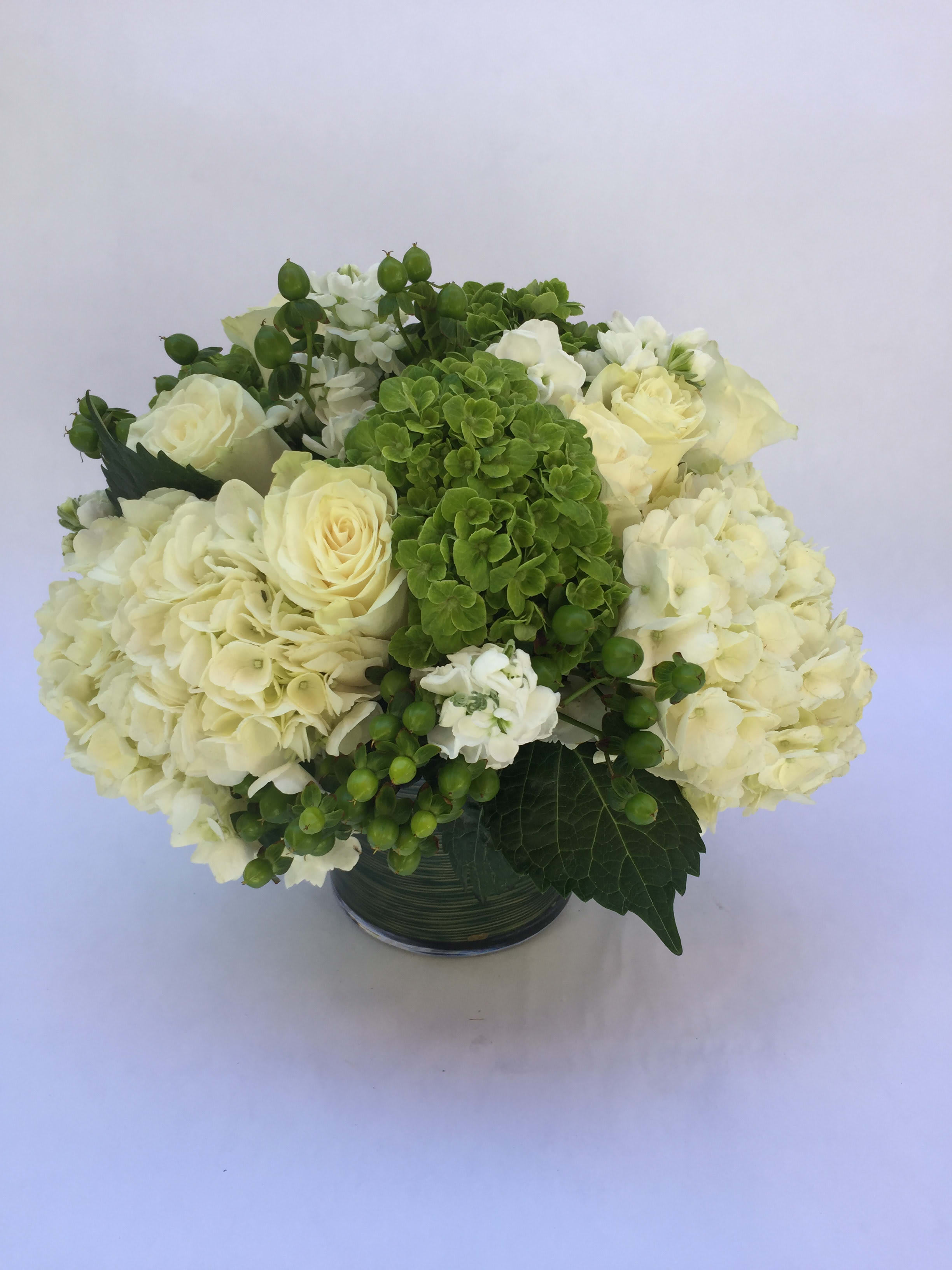 White roses and hydrangeas arranged in a glass vase with green accents