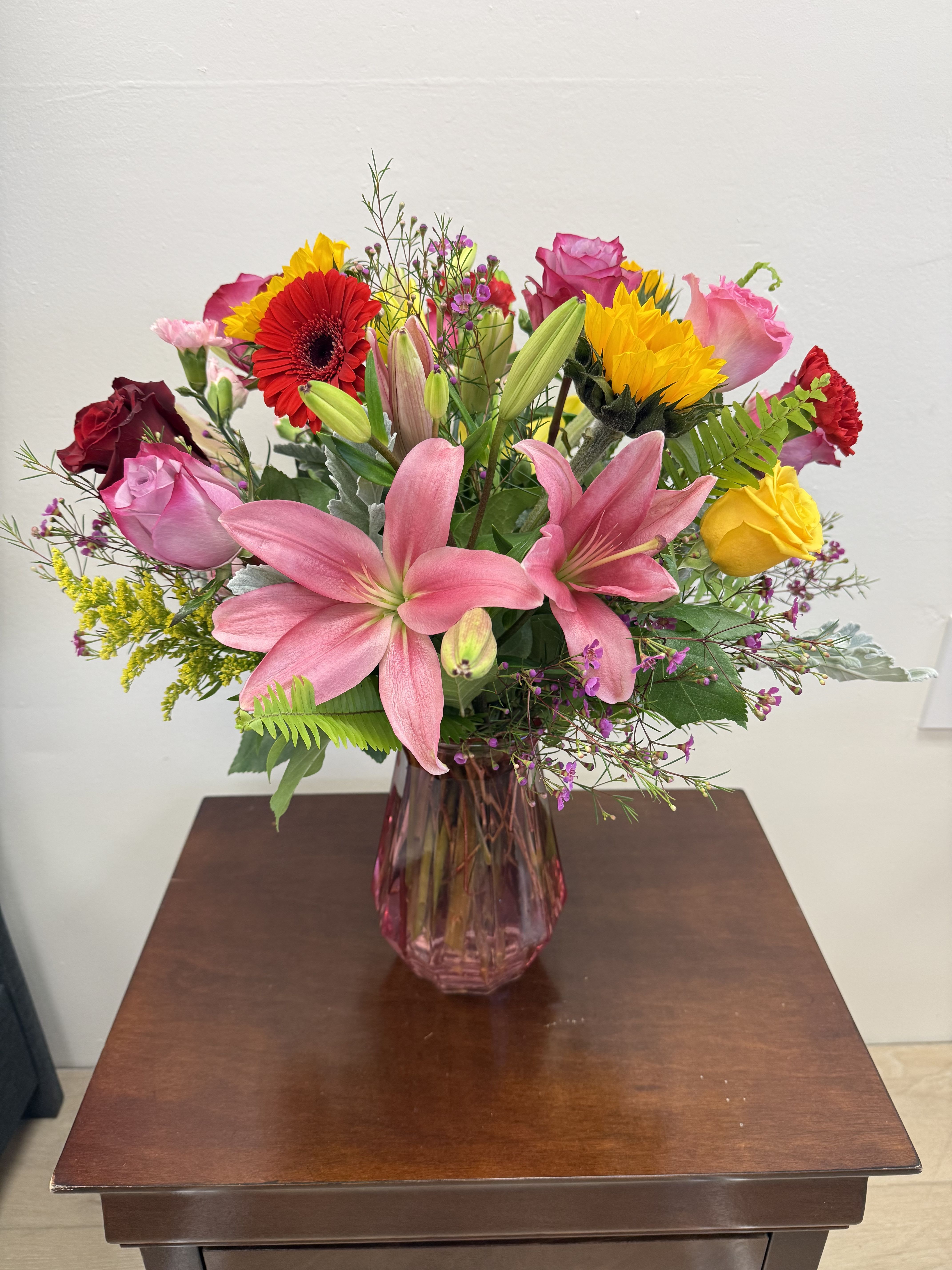 Mixed bouquet of pink lilies, roses, and bright gerbera daisies in a pink vase