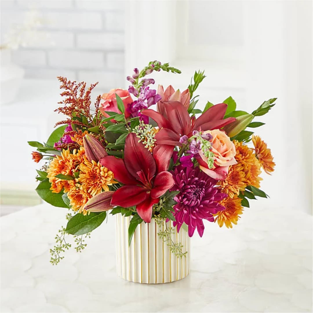 Mixed bouquet of lilies, roses, and mums in a striped vase