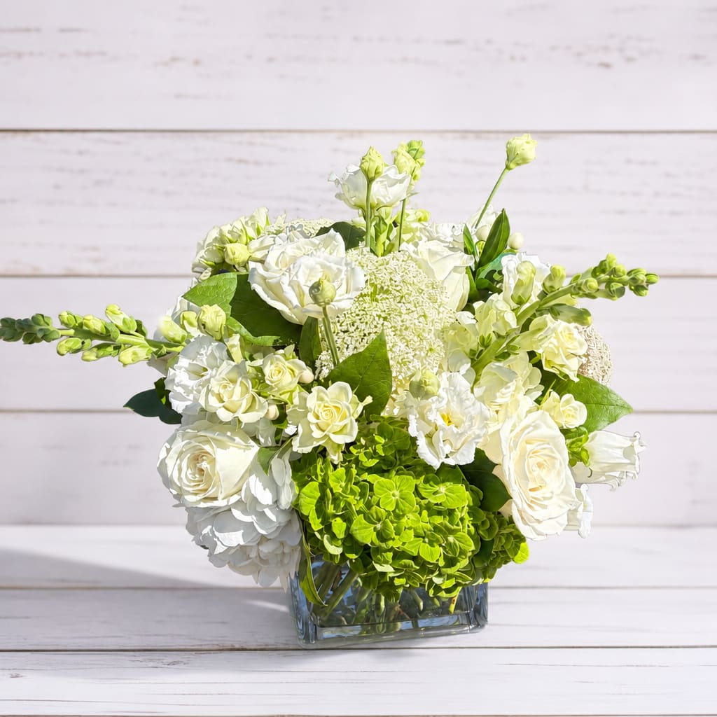 White and green floral arrangement in a square glass vase