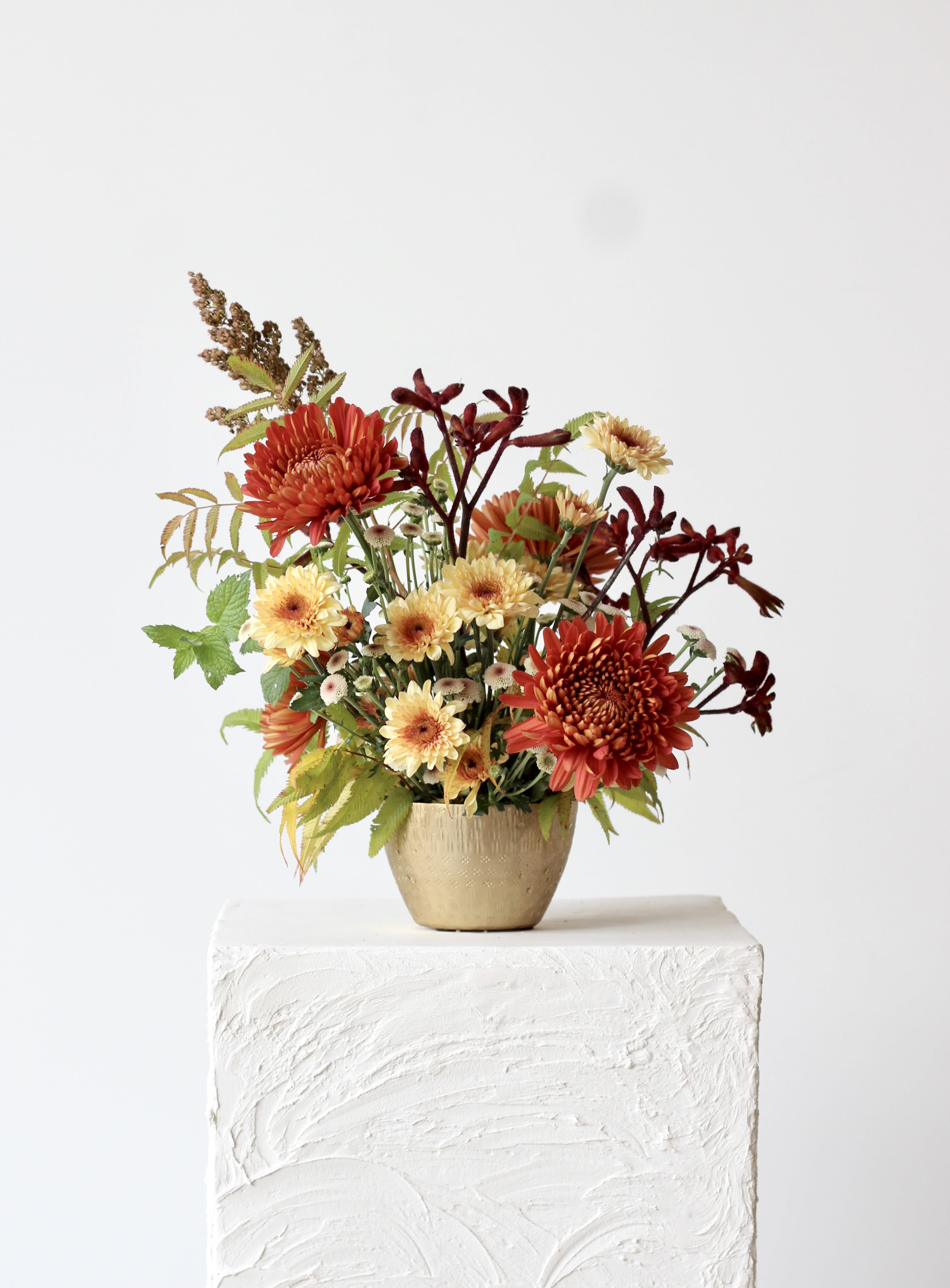 Autumn flower arrangement in a gold vase with red and cream blooms