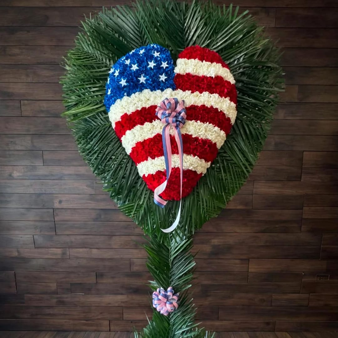 Heart-shaped floral tribute in red, white, and blue with ribbon accents