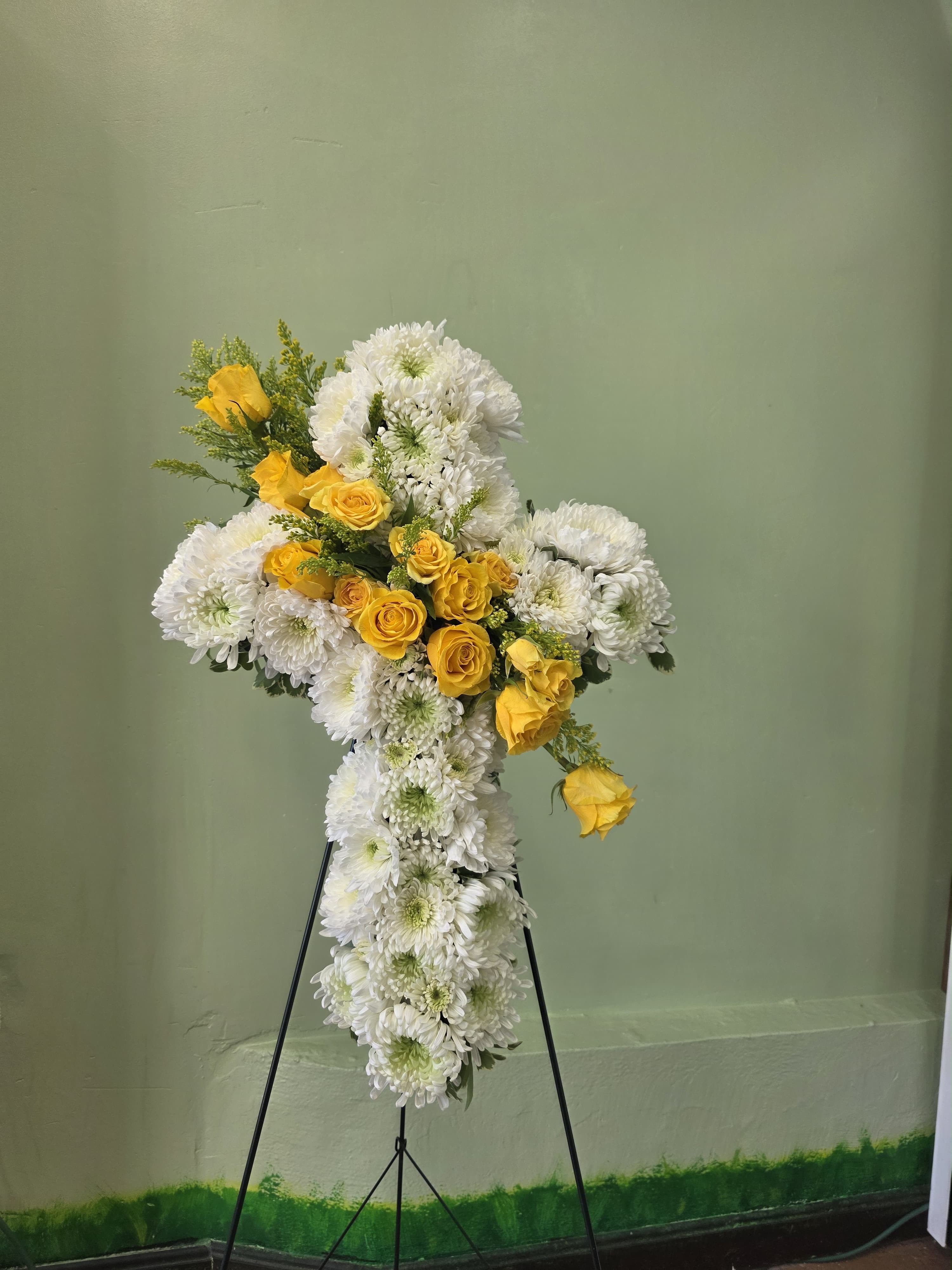 Radiant Remembrance Cross - A dignified standing spray shaped like a cross, crafted to offer comfort and quiet beauty at a funeral or memorial service. The Radiant Remembrance Cross features a classic sympathy arrangement design-white chrysanthemums form the full, layered cross while clusters of yellow roses add a gentle, hopeful contrast that draws the eye and lifts the composition.
