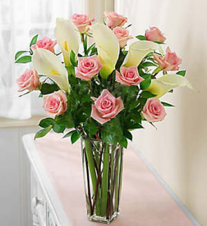 Pink roses and white calla lilies in a tall glass vase