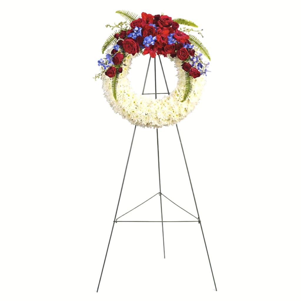 Standing funeral wreath with red roses, white flowers, and blue accents on an easel