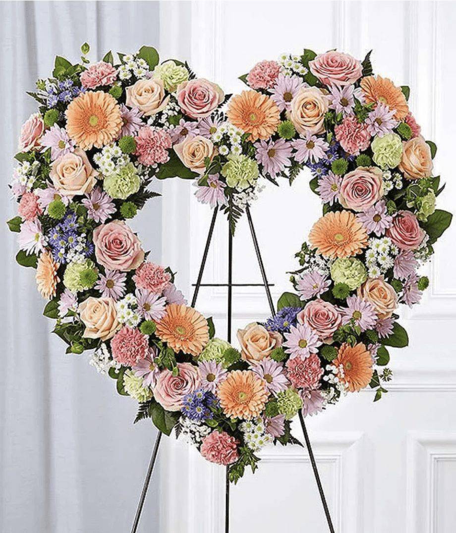 Heart-shaped floral wreath on an easel with pink, peach, and lavender blooms
