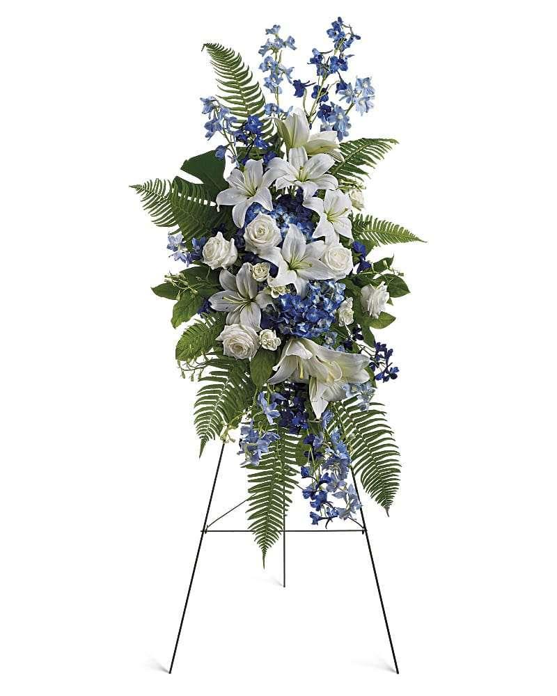 Standing floral spray with white lilies, roses, and blue flowers on an easel