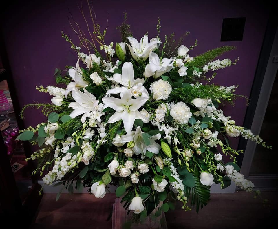 Large all-white floral arrangement with lilies, roses, and other blooms in a fan shape.