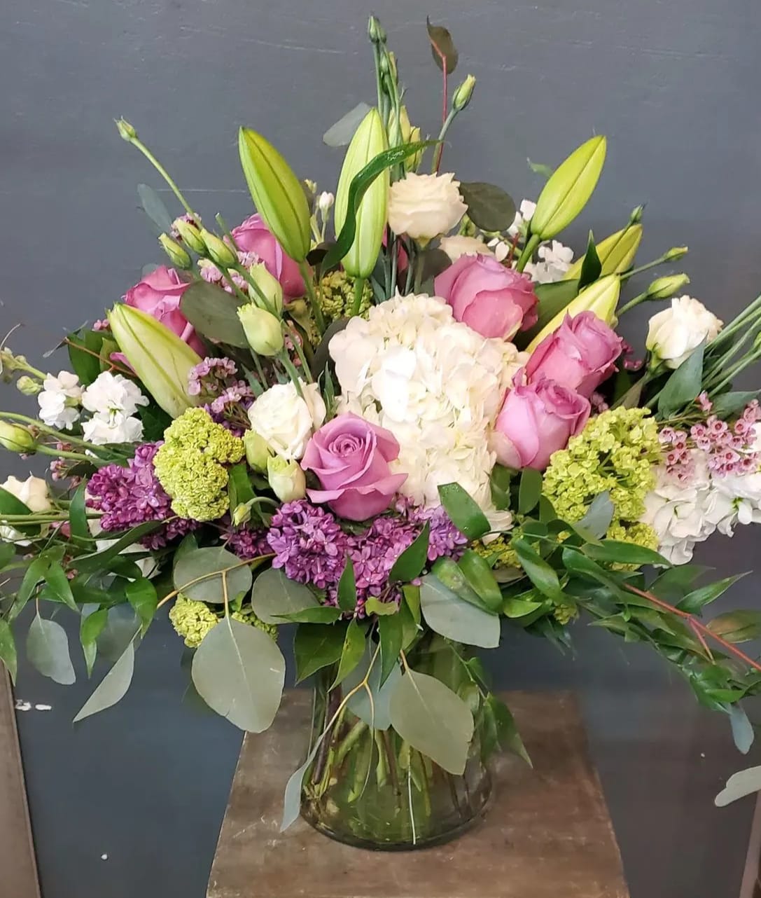 Tall mixed bouquet of pink roses, white hydrangeas, and lilies in a clear glass vase