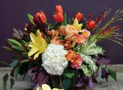 Low arrangement of orange tulips, yellow lilies, white hydrangea, and roses in a container