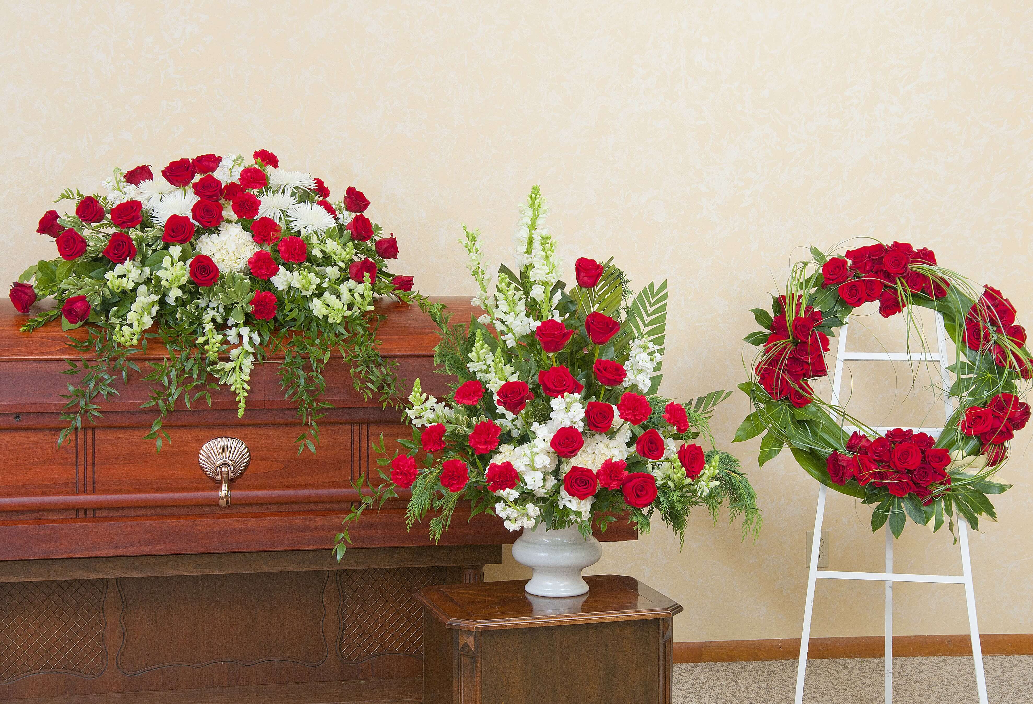 Red and white funeral floral set with casket spray, standing wreath, and tall urn arrangement