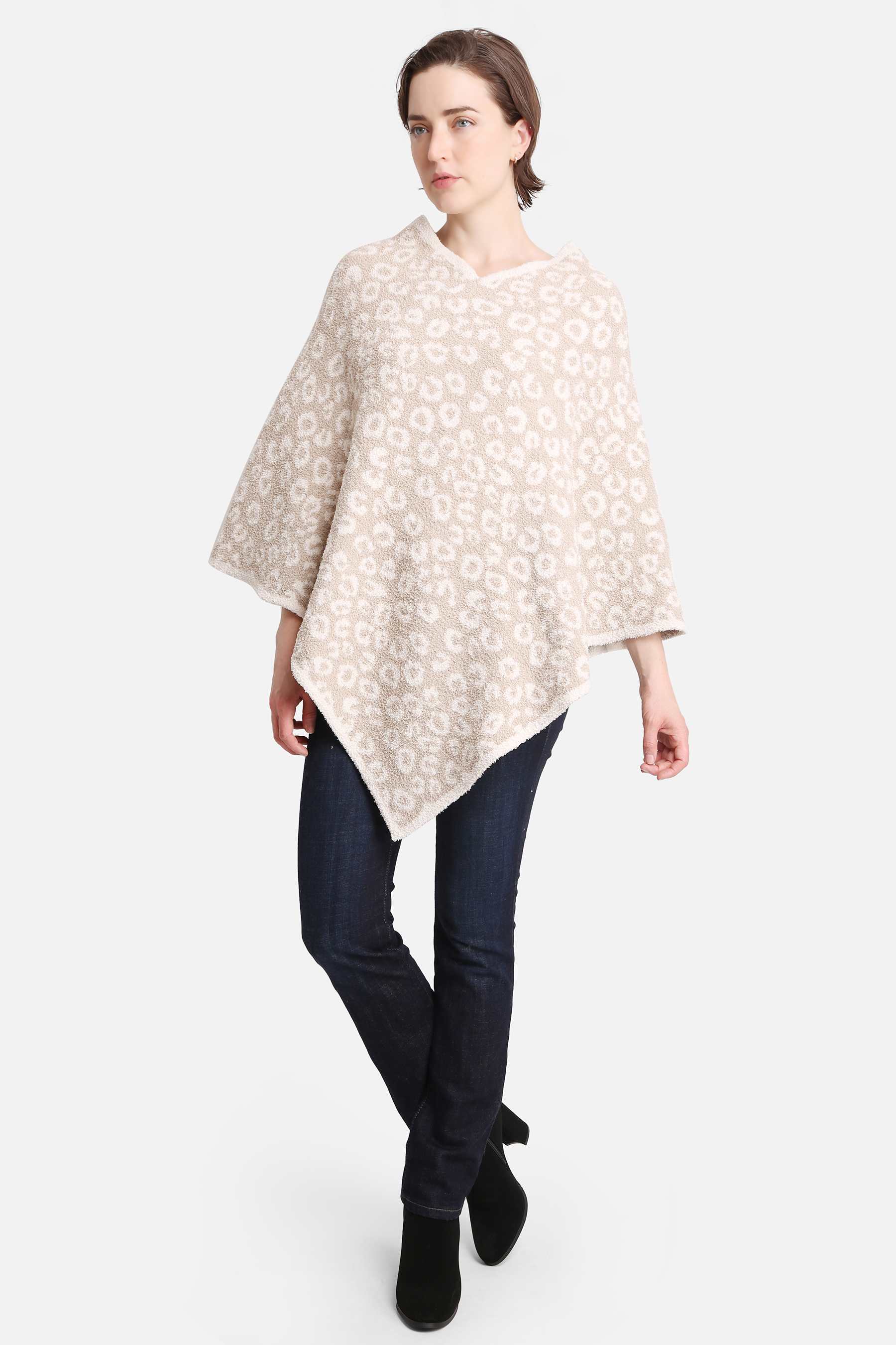 Woman wearing a beige patterned poncho with dark jeans and black ankle boots