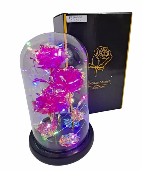 Artificial pink roses with LED lights inside a glass dome on a black base beside a black gift box
