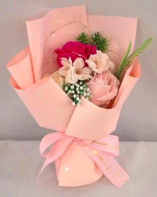Small bouquet of pink and white roses and blossoms wrapped in pale pink paper with a bow