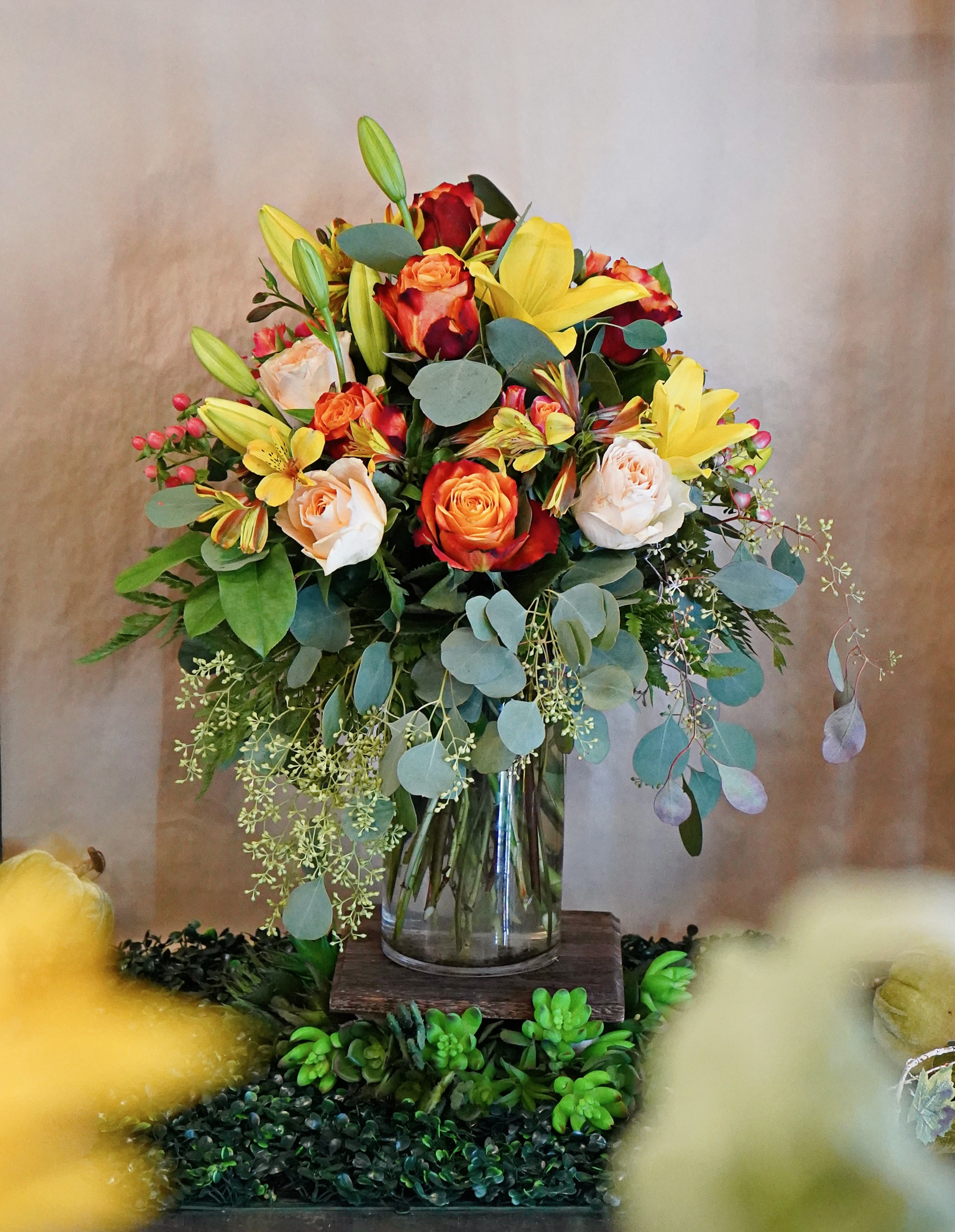 Tall bouquet of orange roses and yellow lilies with cream roses in a clear glass vase