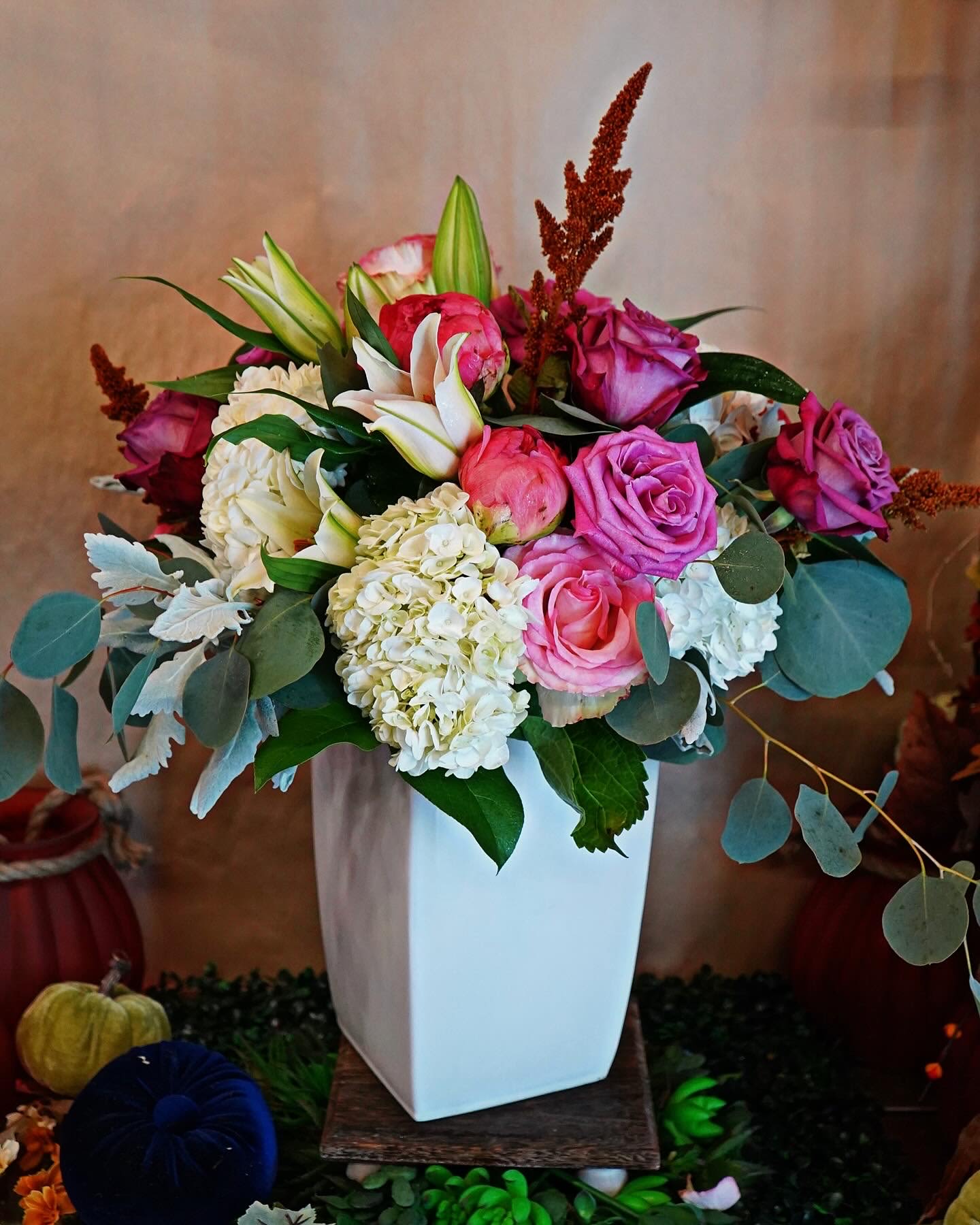 Tall white vase of pink roses, white hydrangeas, and lilies in a mixed arrangement