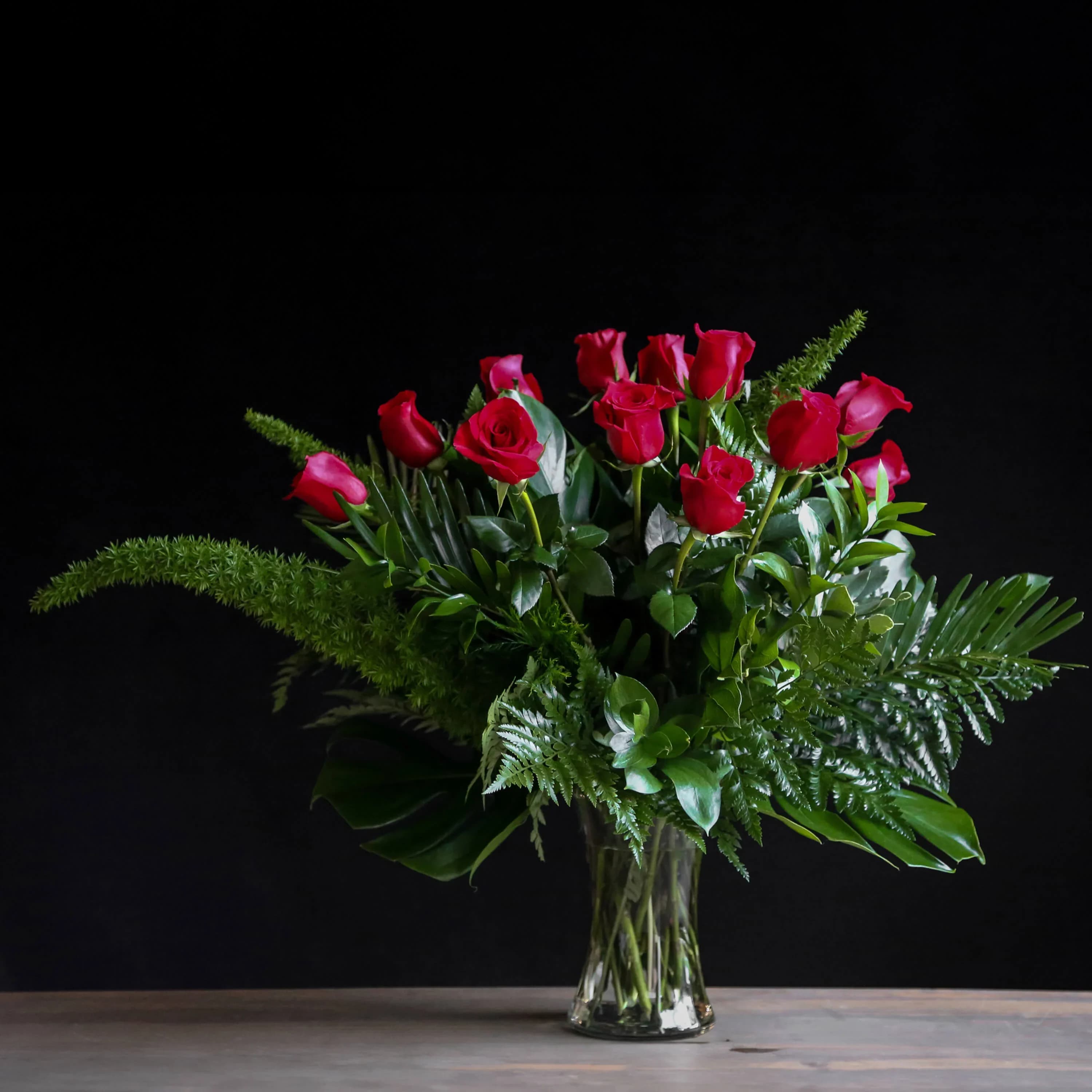 Arrangement of long-stemmed red roses with abundant foliage in a clear glass vase