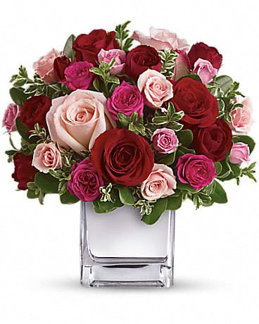 Short arrangement of red and pink roses in a clear glass cube vase