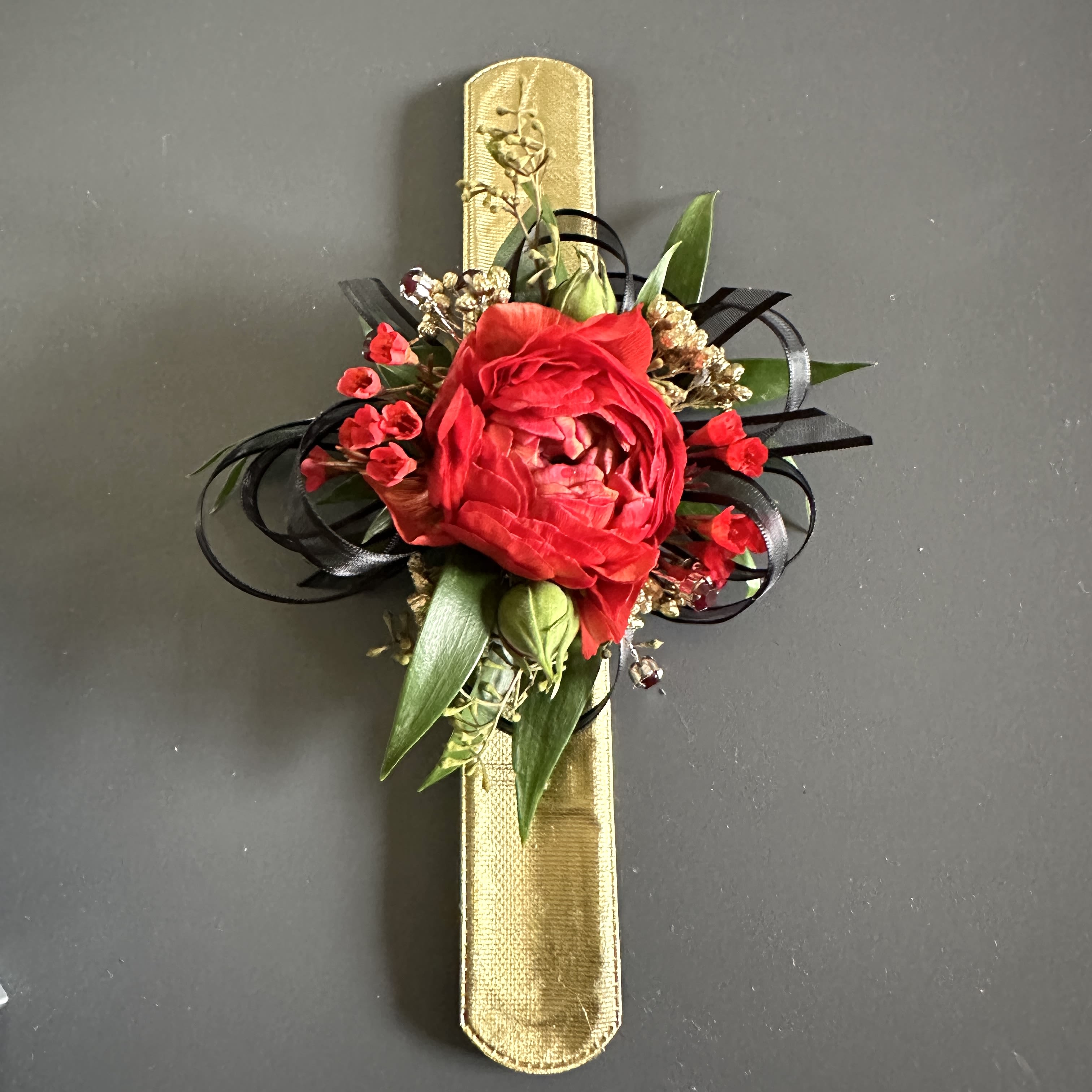 Red floral corsage on a gold ribbon band with black ribbon loops