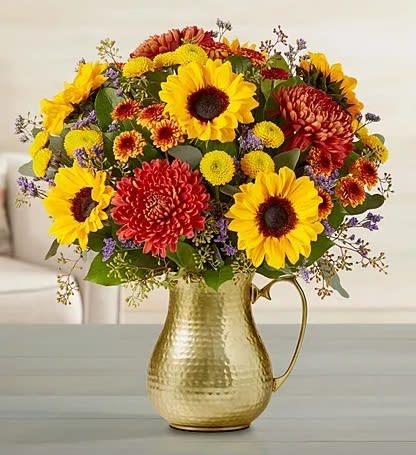 Yellow sunflowers and orange mums arranged in a hammered gold metal pitcher