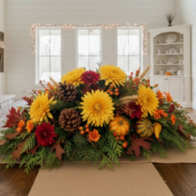Low fall centerpiece with yellow and red mums, pinecones, berries, and mini pumpkins on a table runner