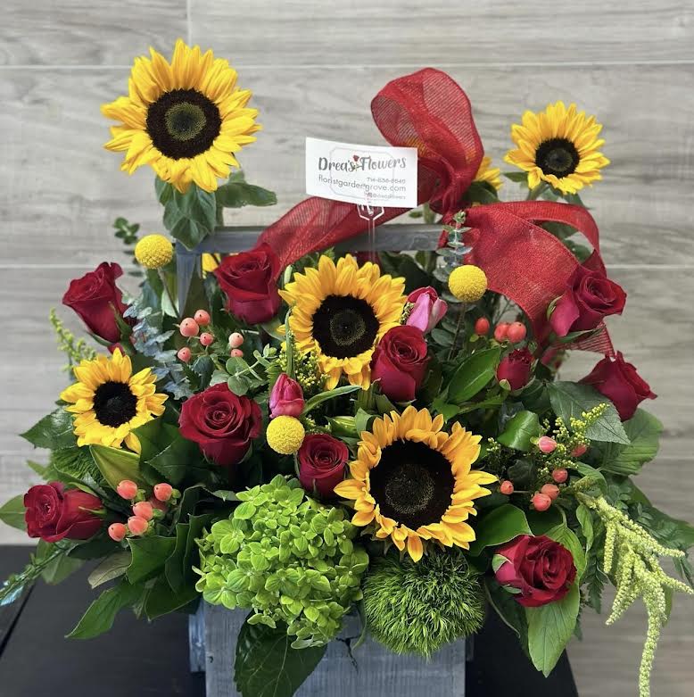 Sunflowers and red roses arranged with a red ribbon in a square container