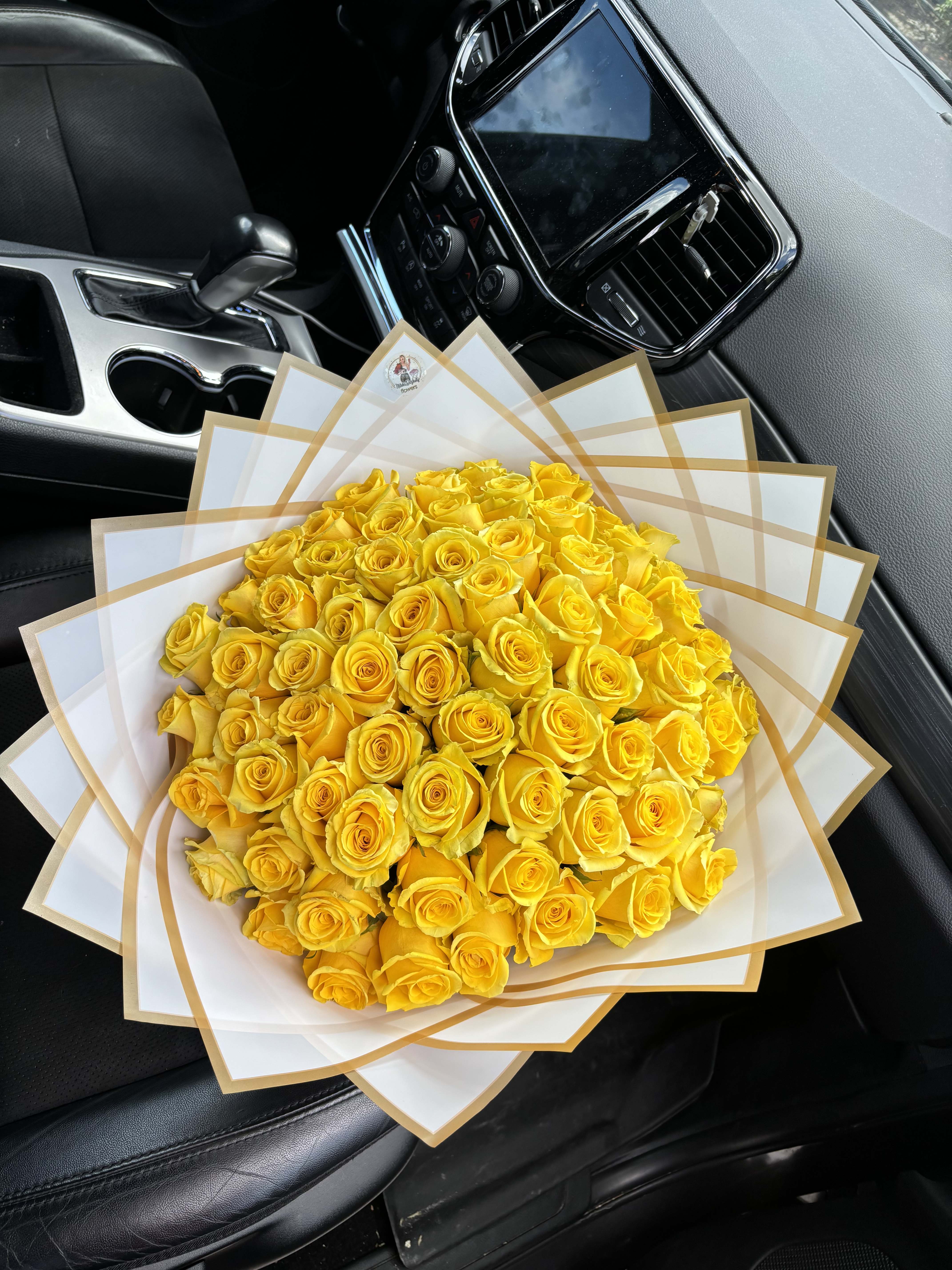 Large bouquet of yellow roses wrapped in white paper with gold trim