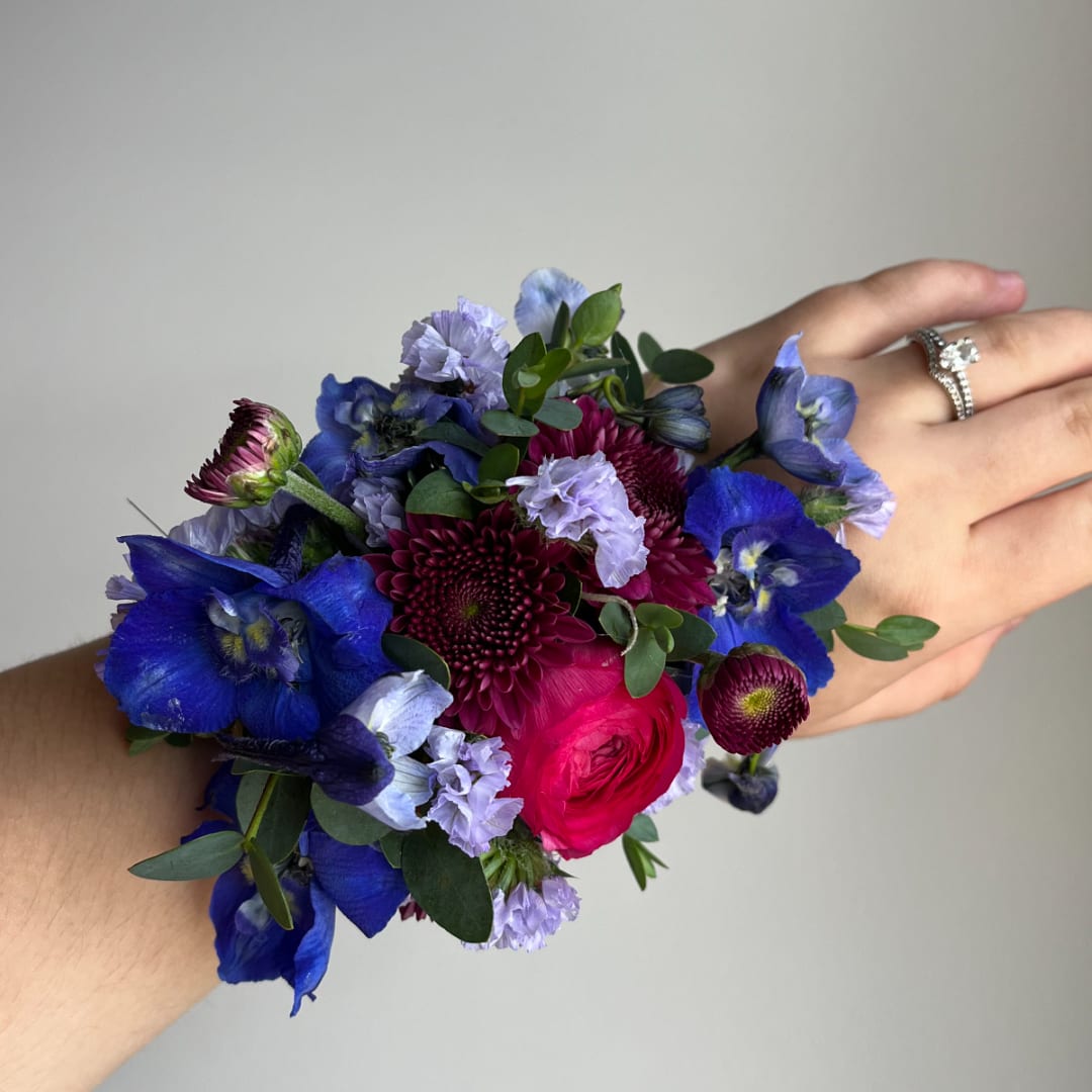Handheld wrist corsage with blue and purple flowers and a pink rose