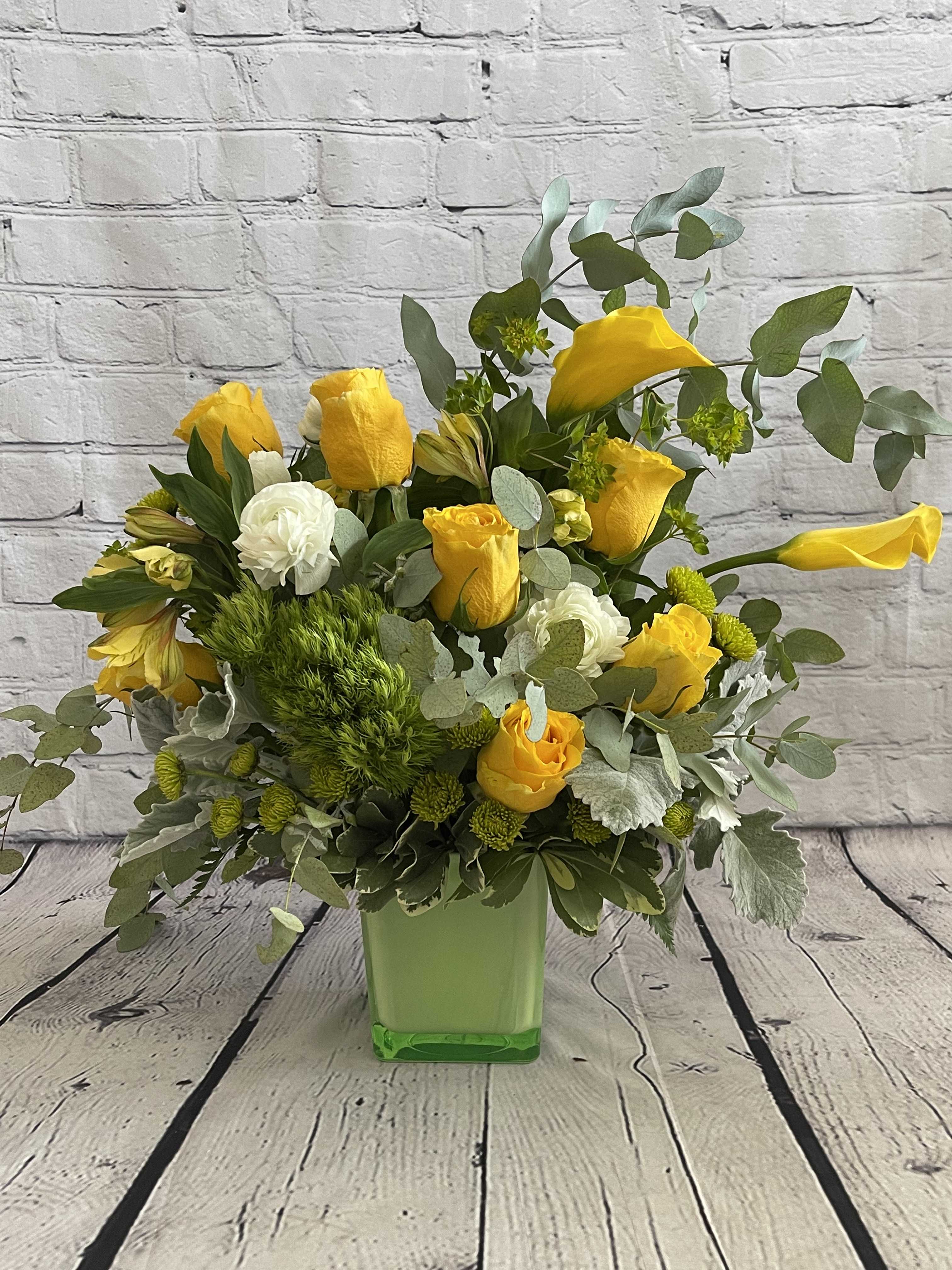 Yellow roses and white blooms arranged in a green square vase