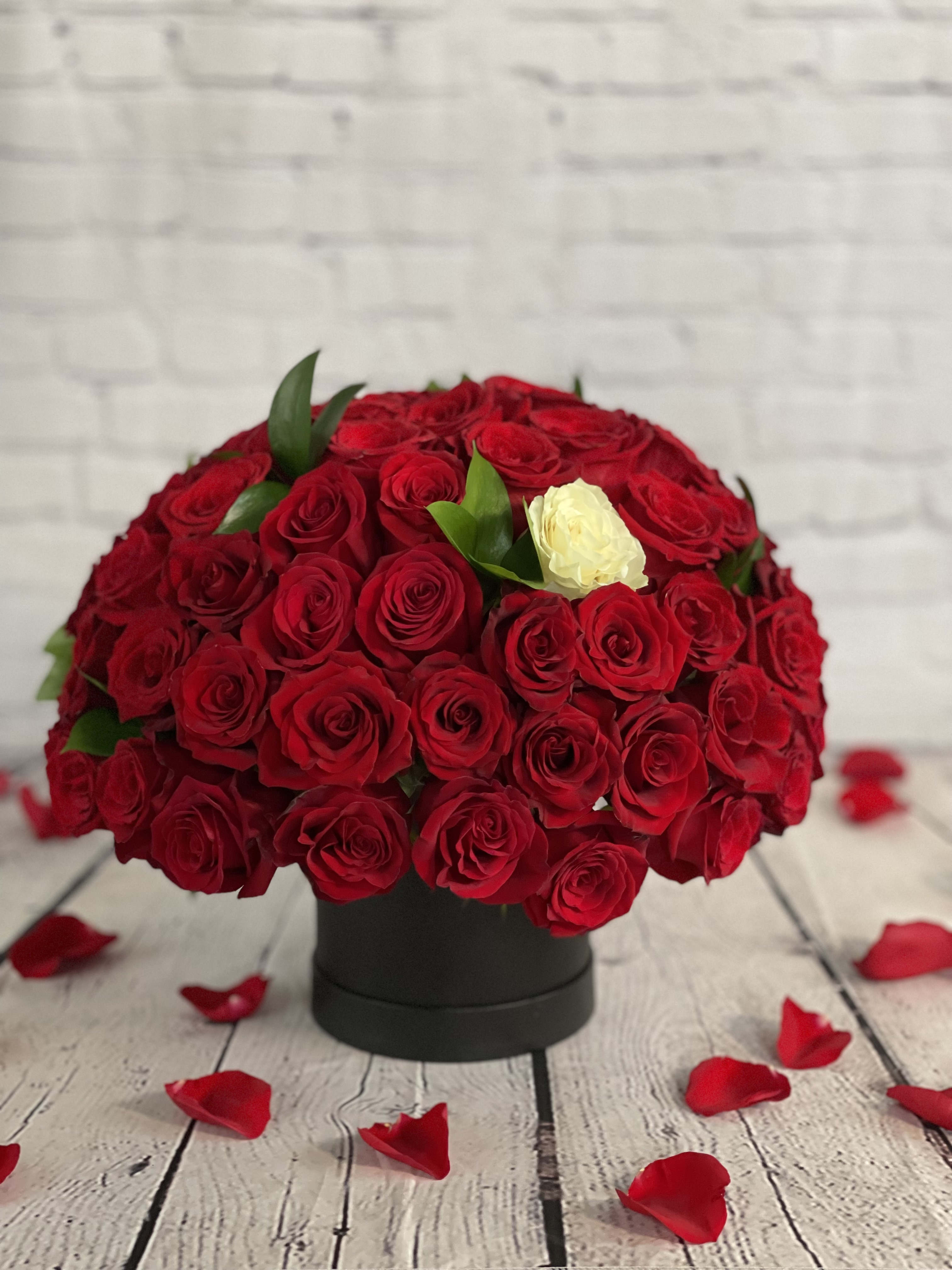 Round bouquet of red roses with one white rose in a black box