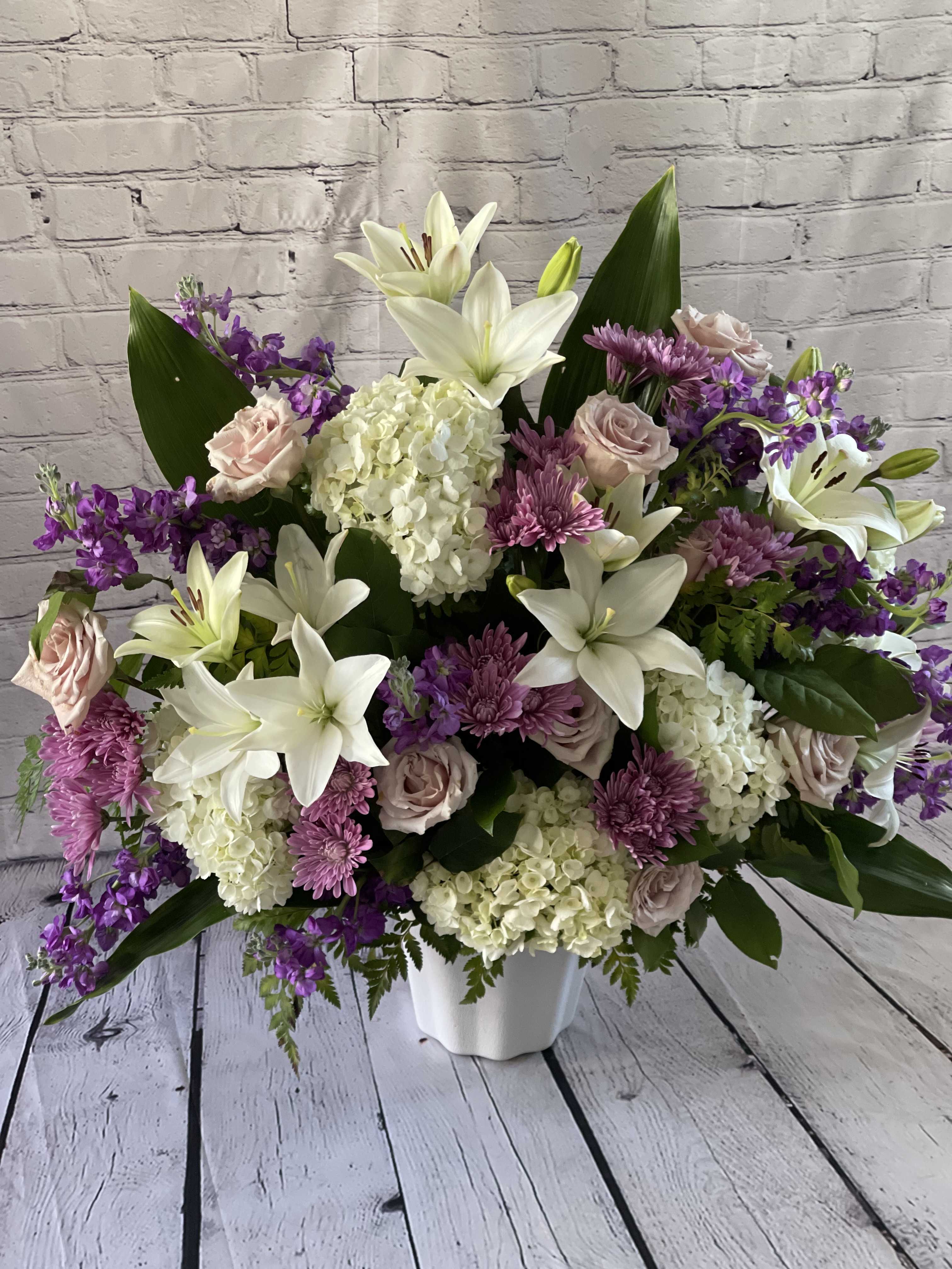 Large bouquet of white lilies, pink roses, and purple flowers in a white vase
