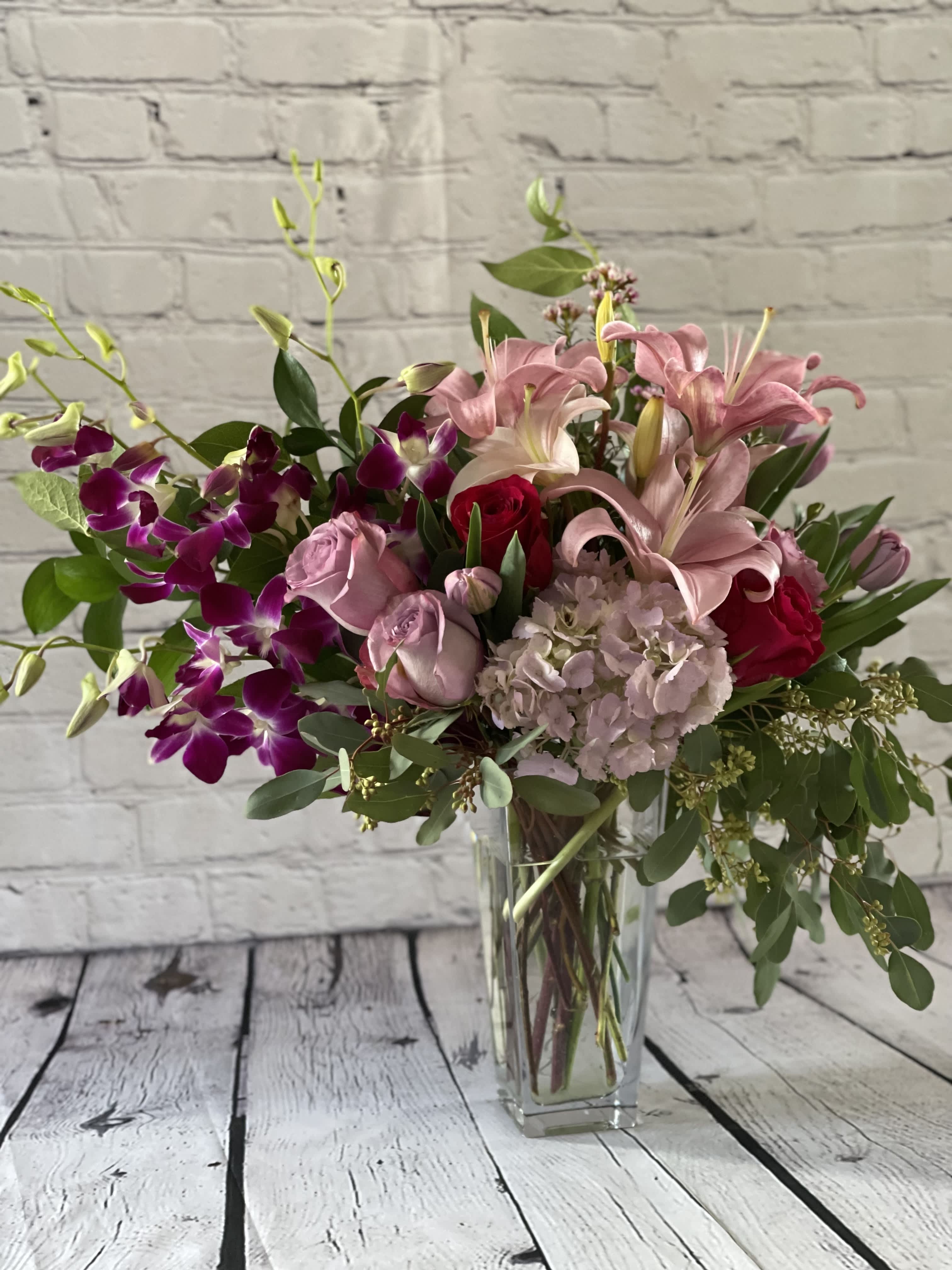 Pink lilies and roses in a clear glass vase with purple orchids