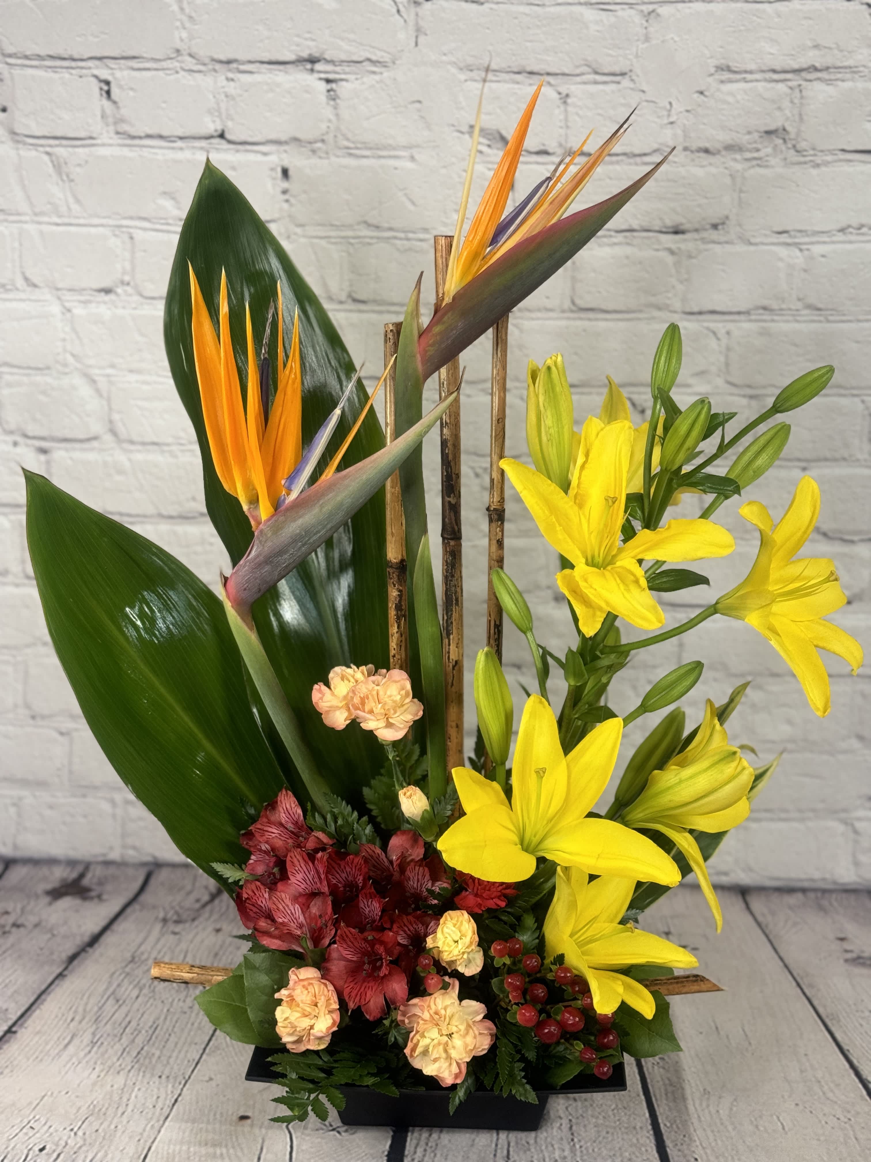 Tropical flower arrangement with yellow lilies and bird of paradise in a black container