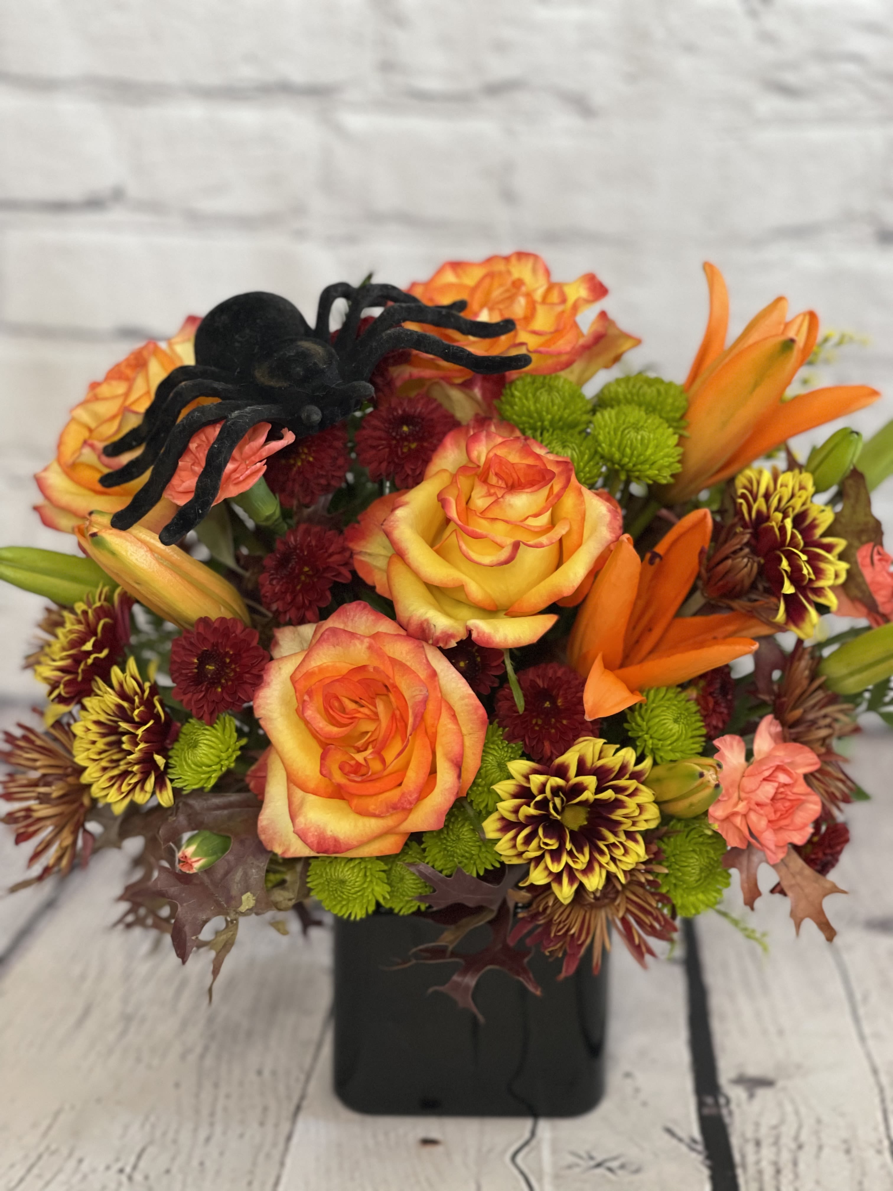 Orange roses and mixed mums in a black vase with a decorative spider accent