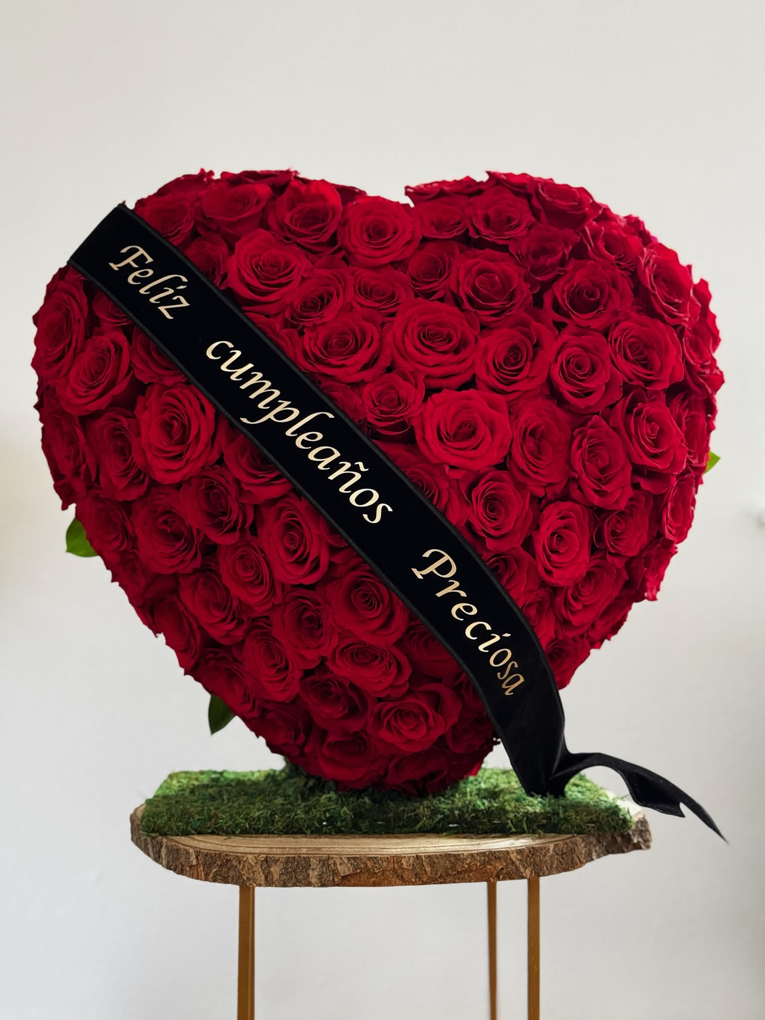 Heart-shaped red rose arrangement with a black ribbon on a wood slab stand