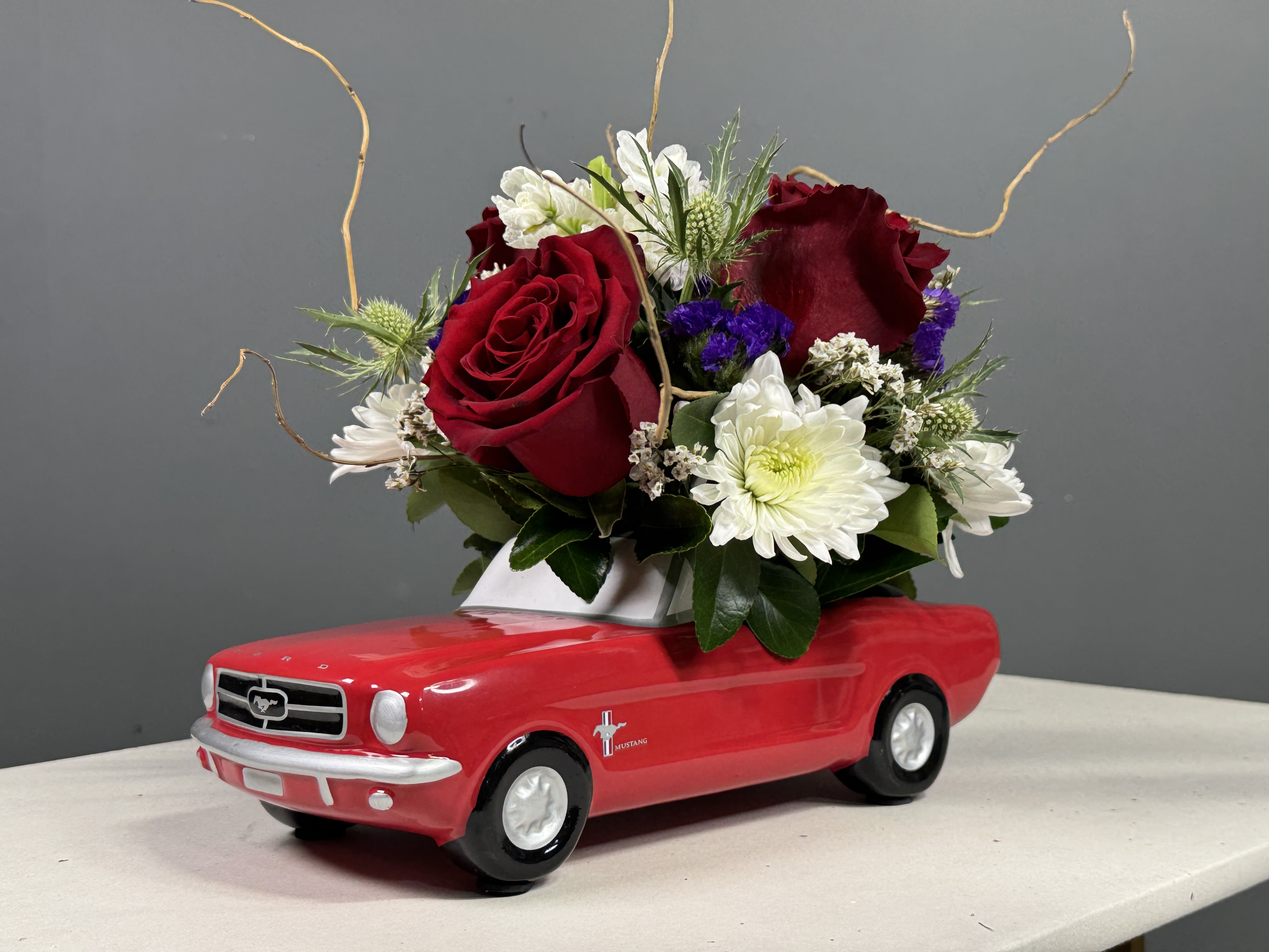 Red roses and white daisies arranged in a red toy car