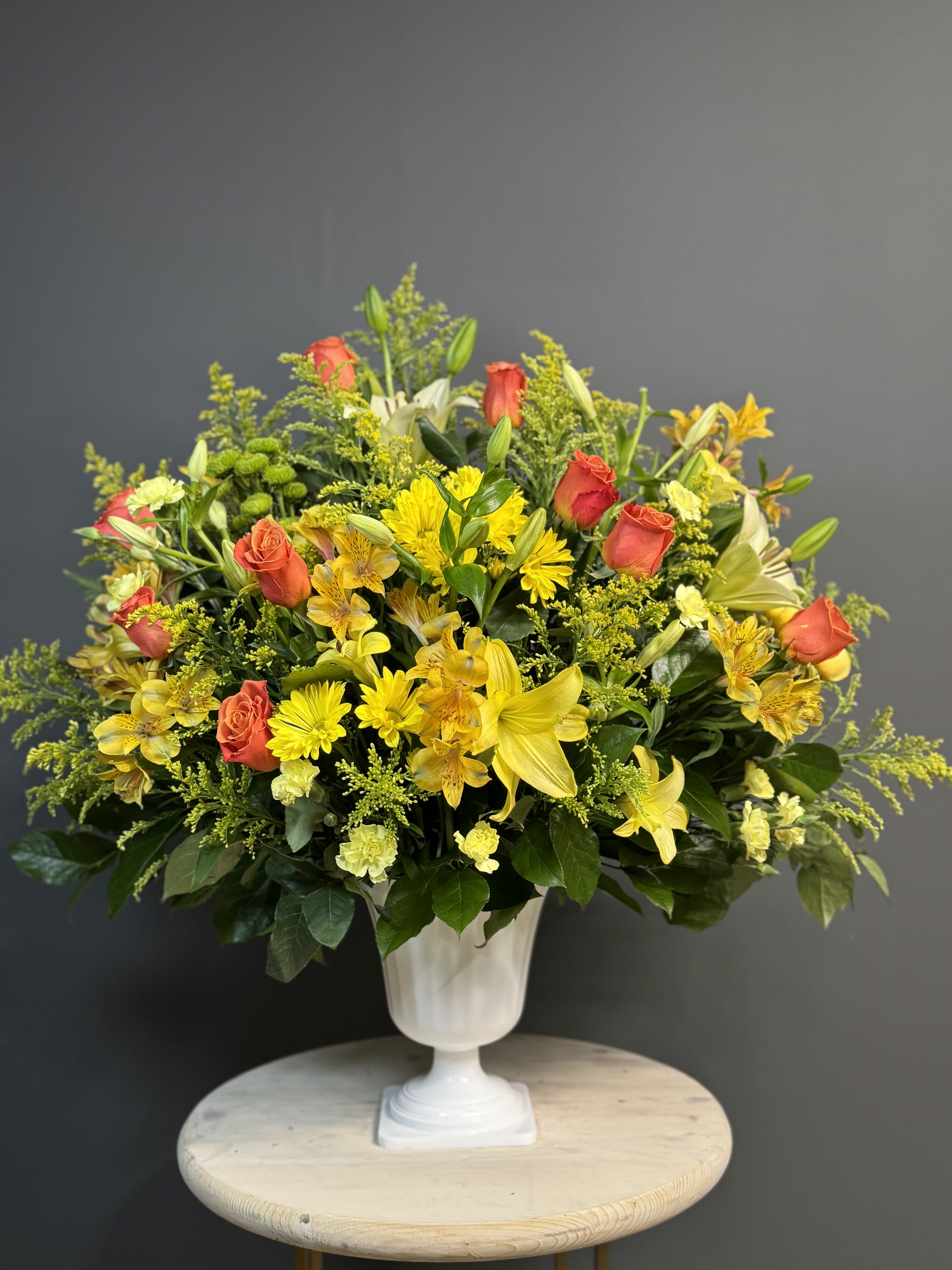 Yellow and coral mixed flower arrangement in a white pedestal vase