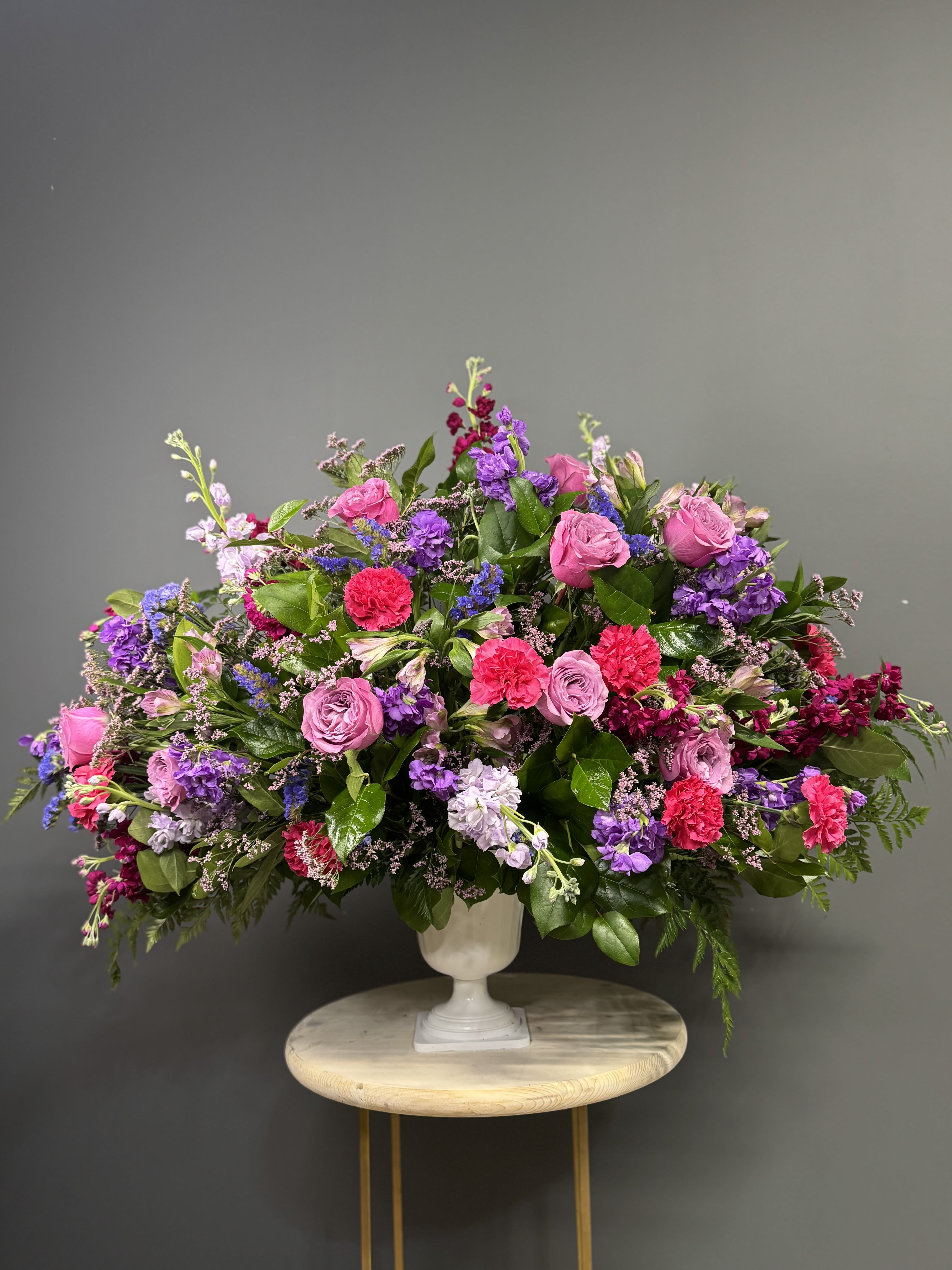 Large mixed bouquet of pink, purple, and red flowers in a white urn vase