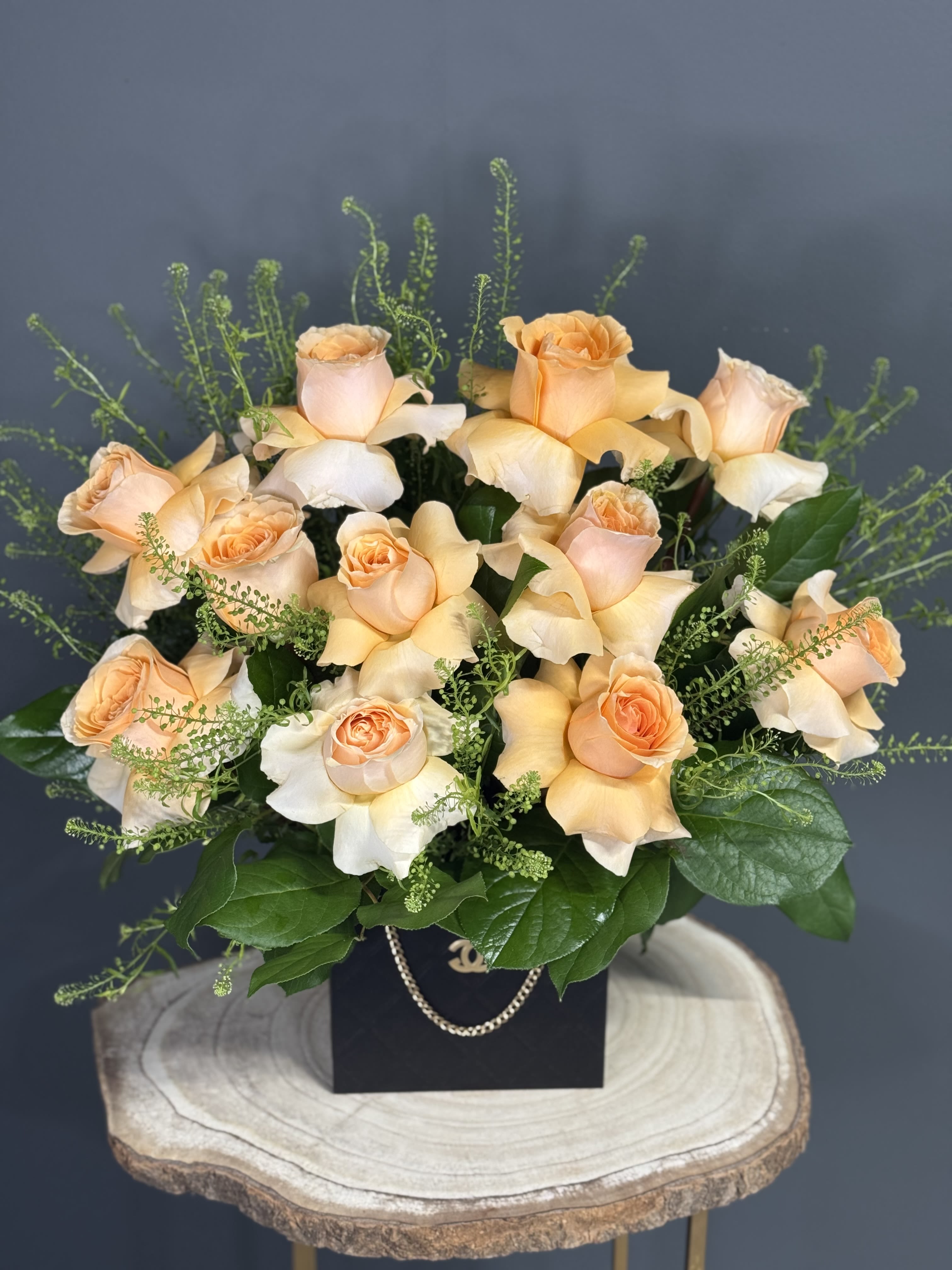 Peach roses arranged in a black box with greenery