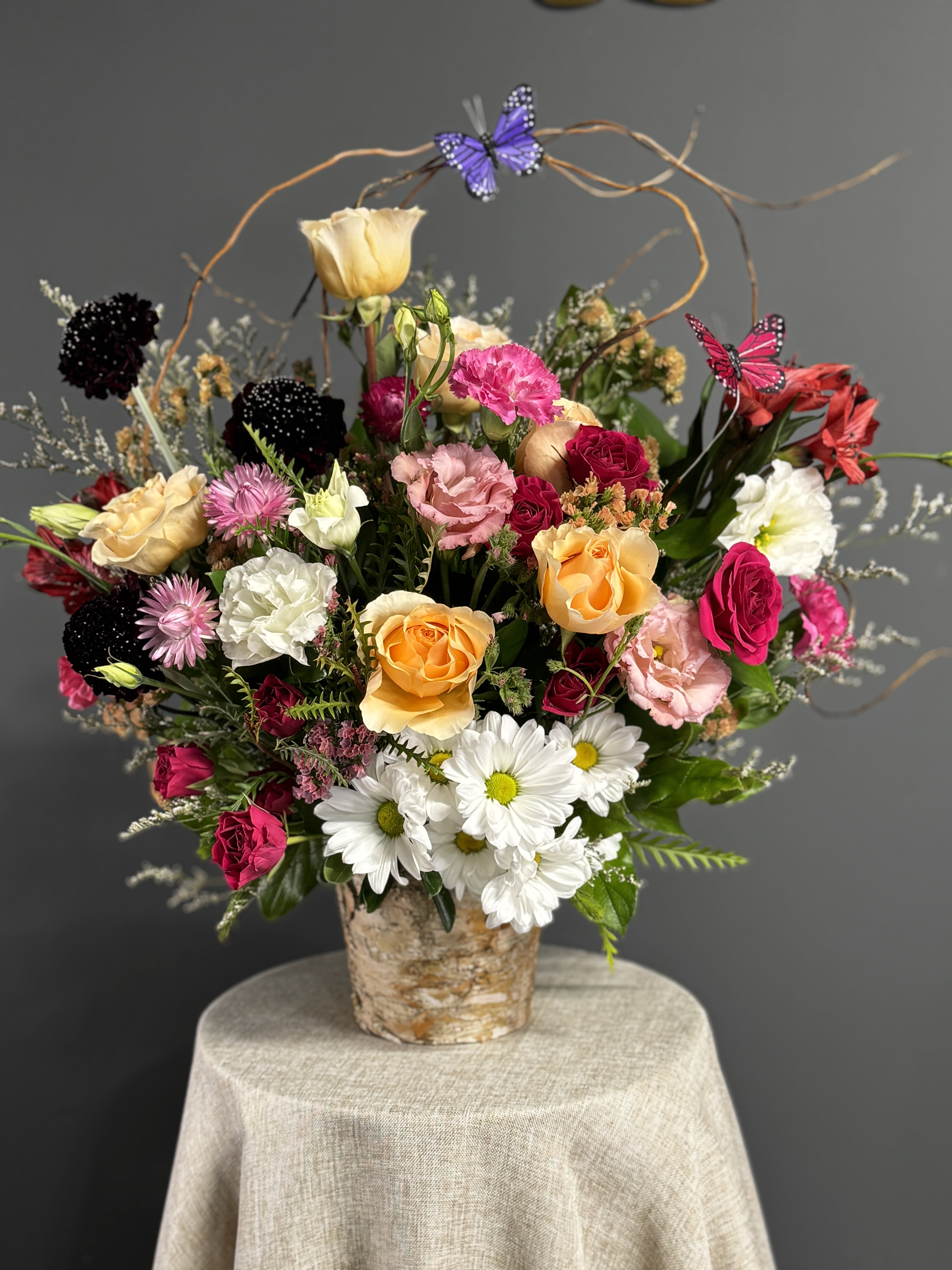 Mixed bouquet of roses, daisies, and carnations in a birch-style container