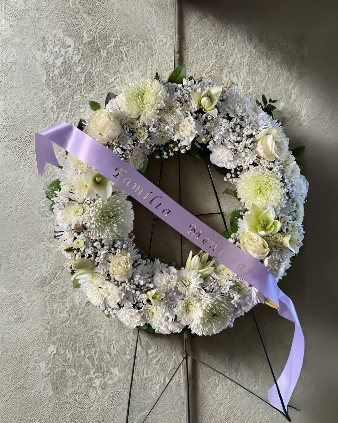 White floral wreath on a stand with a lavender ribbon