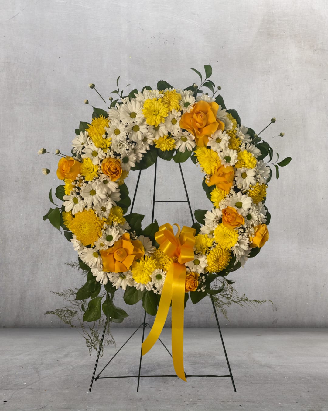 Yellow and white floral wreath on a black stand with a ribbon